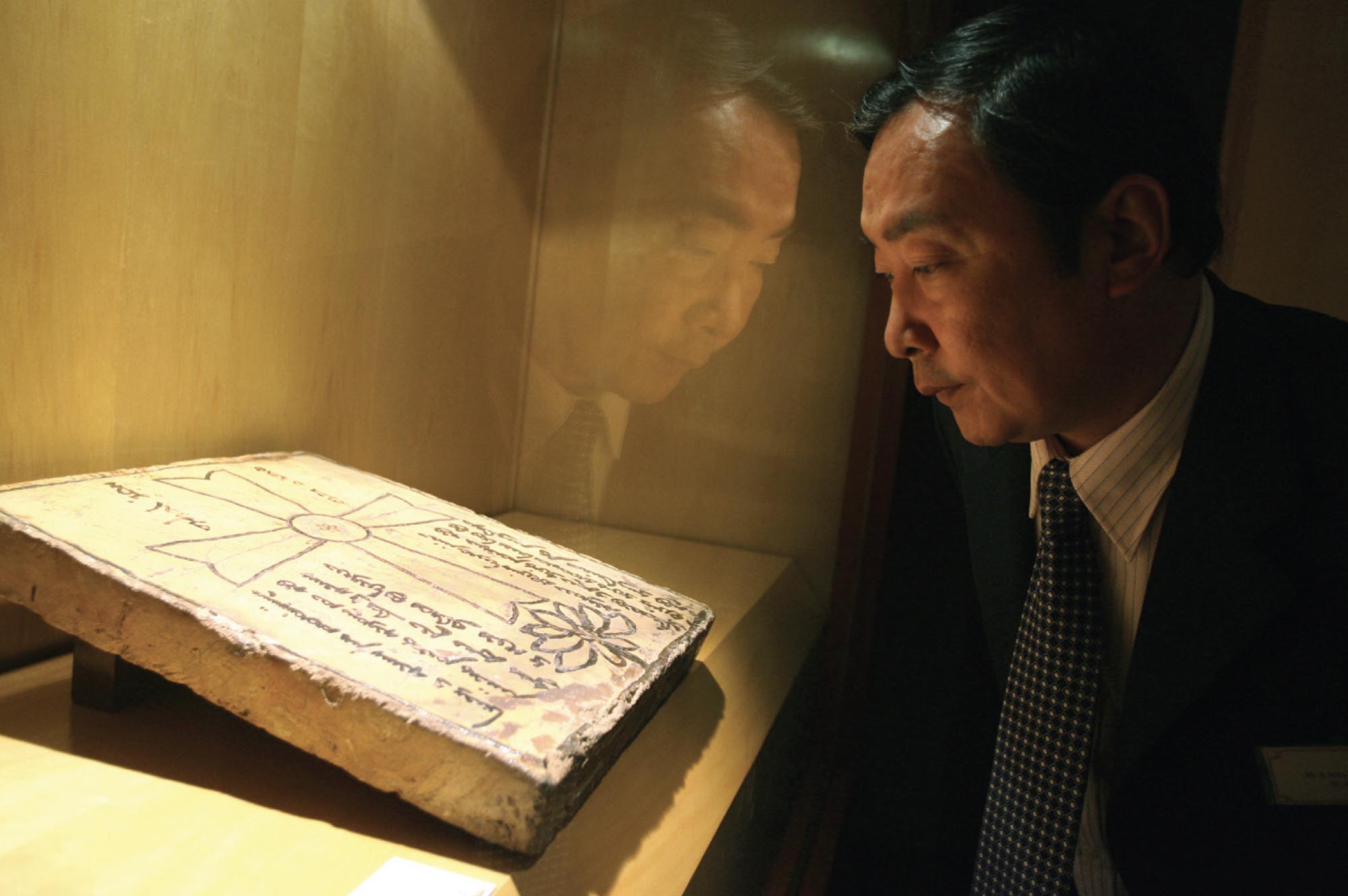 A man looking at a porcelain Nestorian Christrian plaque from the Yuan Dynasty in an exhibition.