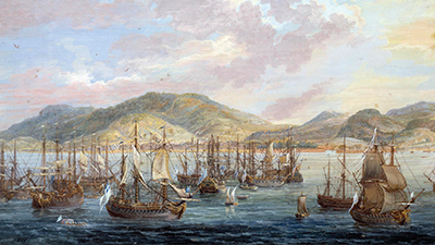Painting of a crowded harbor with sailing ships at anchor with green hills in the background.