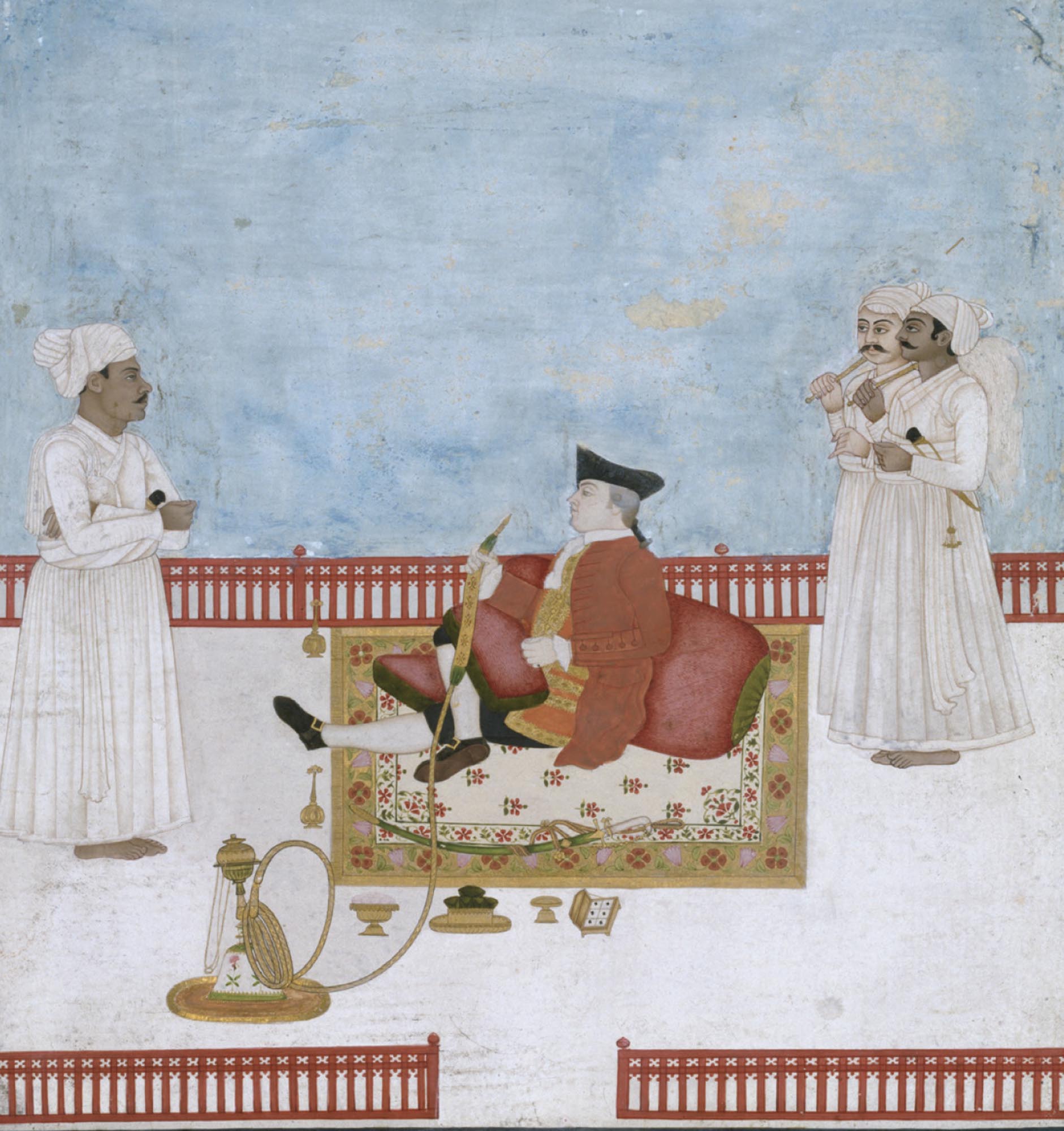 A wealthy British man sits on a carpet and receives a visitor while being attended by servants.