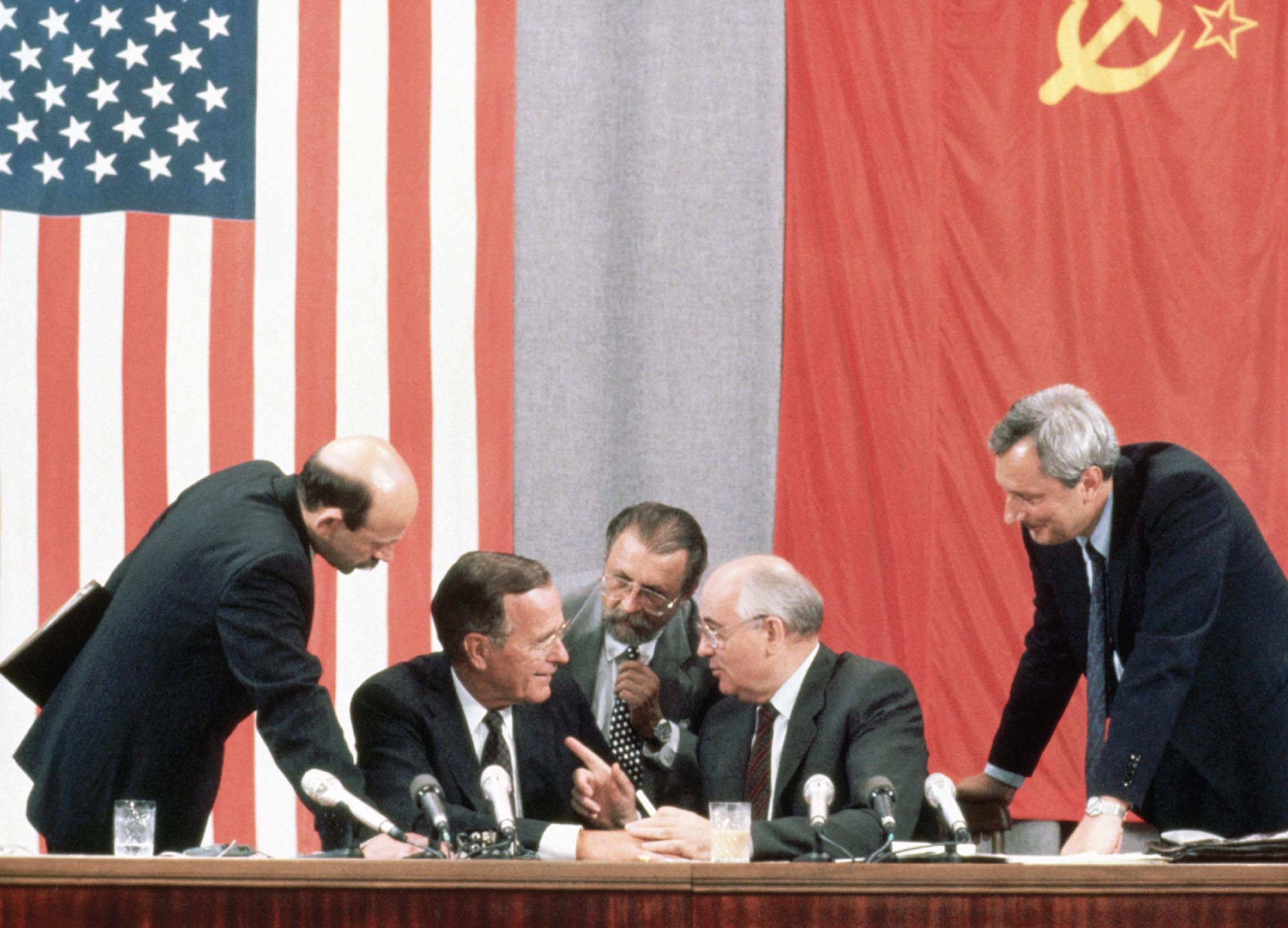 Photo of President George H.W. Bush, Soviet leader Mikhail Gorbachev, and their associates sitting behind a table, deep in conversation. Behind them on the wall are American and Soviet flags.
