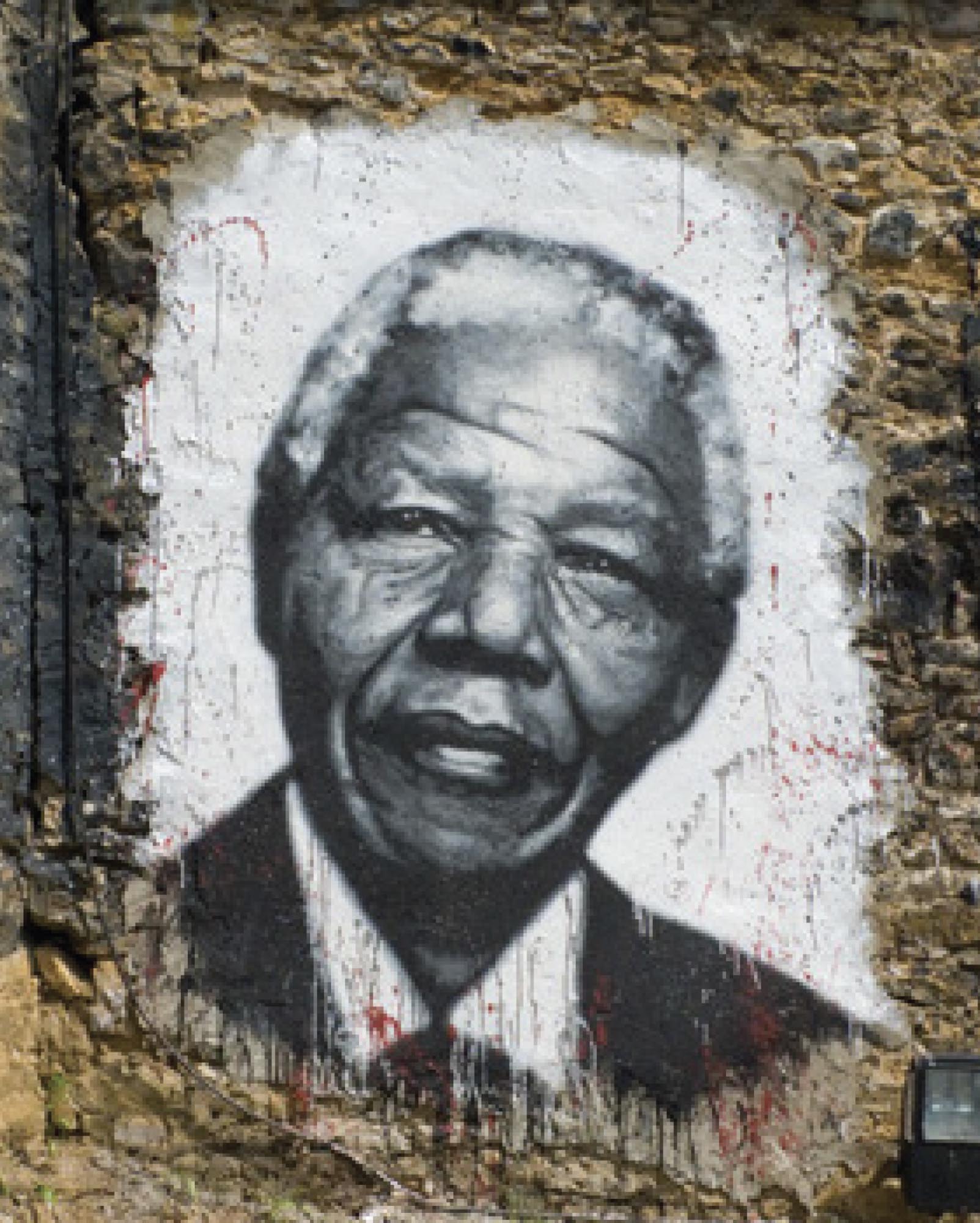 Mural of Nelson Mandela painted over a stone wall. The mural is painted in black and white, and Mandela is depicted wearing a suit.