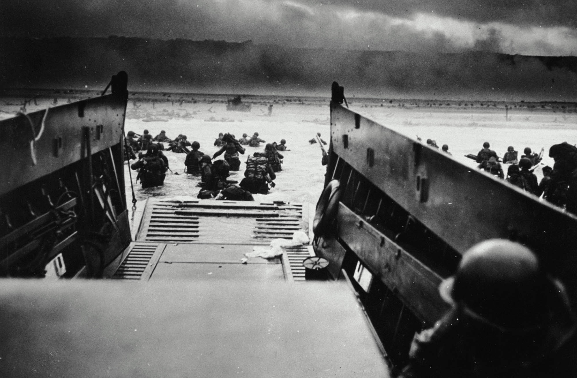 A black and white photograph of U.S. soldiers wading through the ocean waters towards shore.