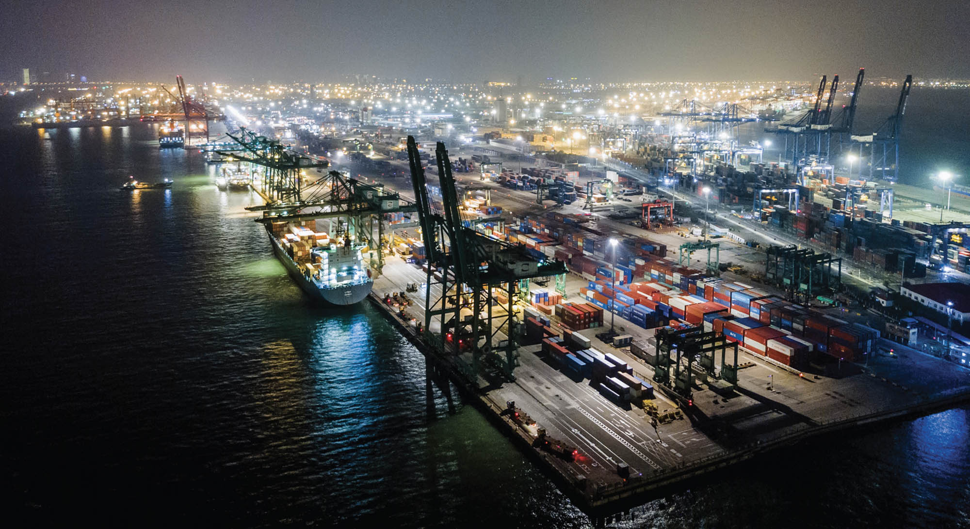 A modern shipping loading harbor with docs and cranes at night.