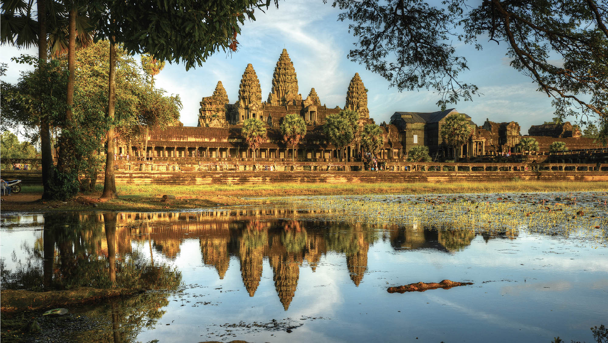 Photo of an old Hindu temple. The temple's reflection can be seen in the still water of the lake in the foreground of the image.