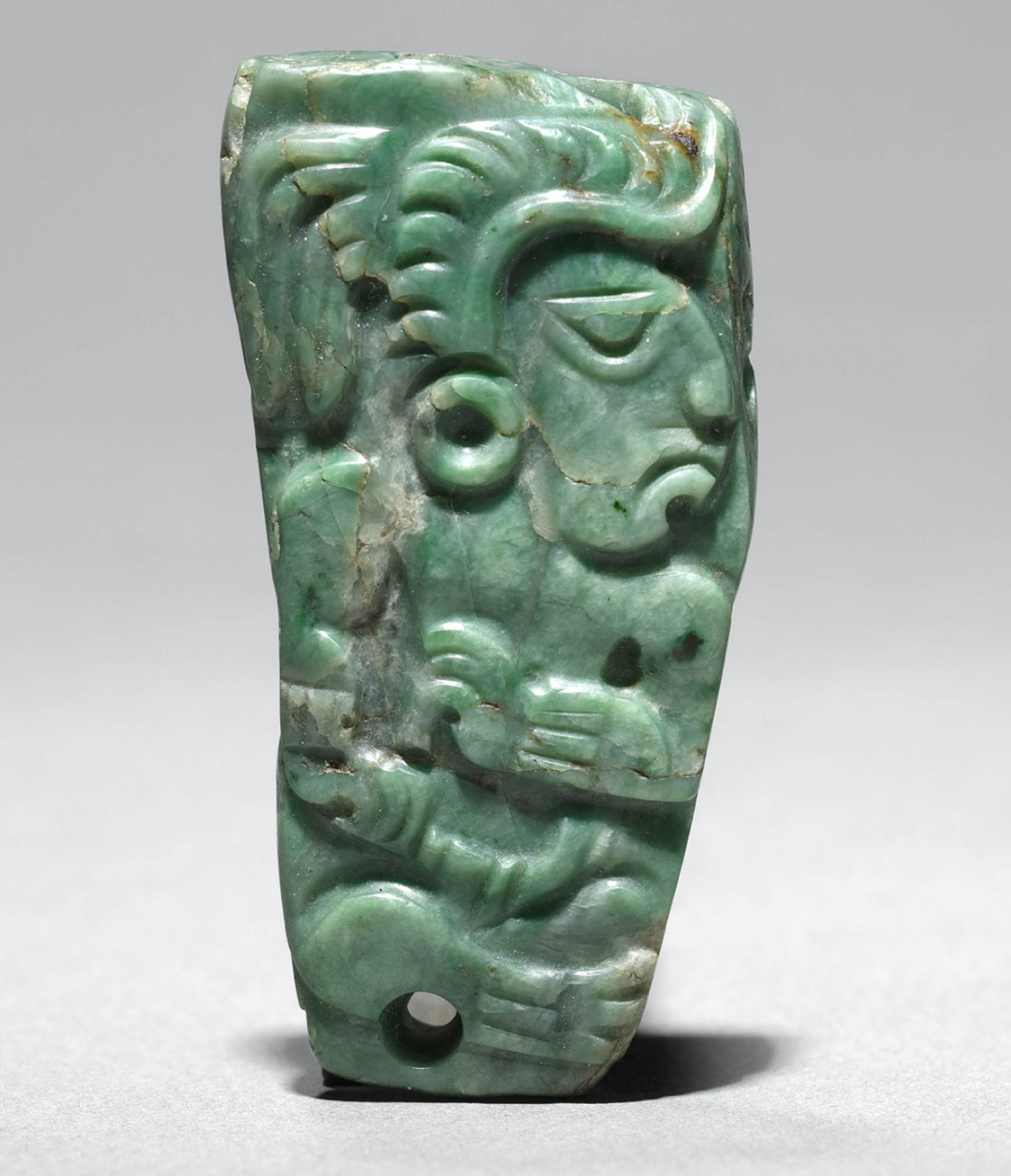 A green jade ornament with a profile view of a Mayan figure carved into it.