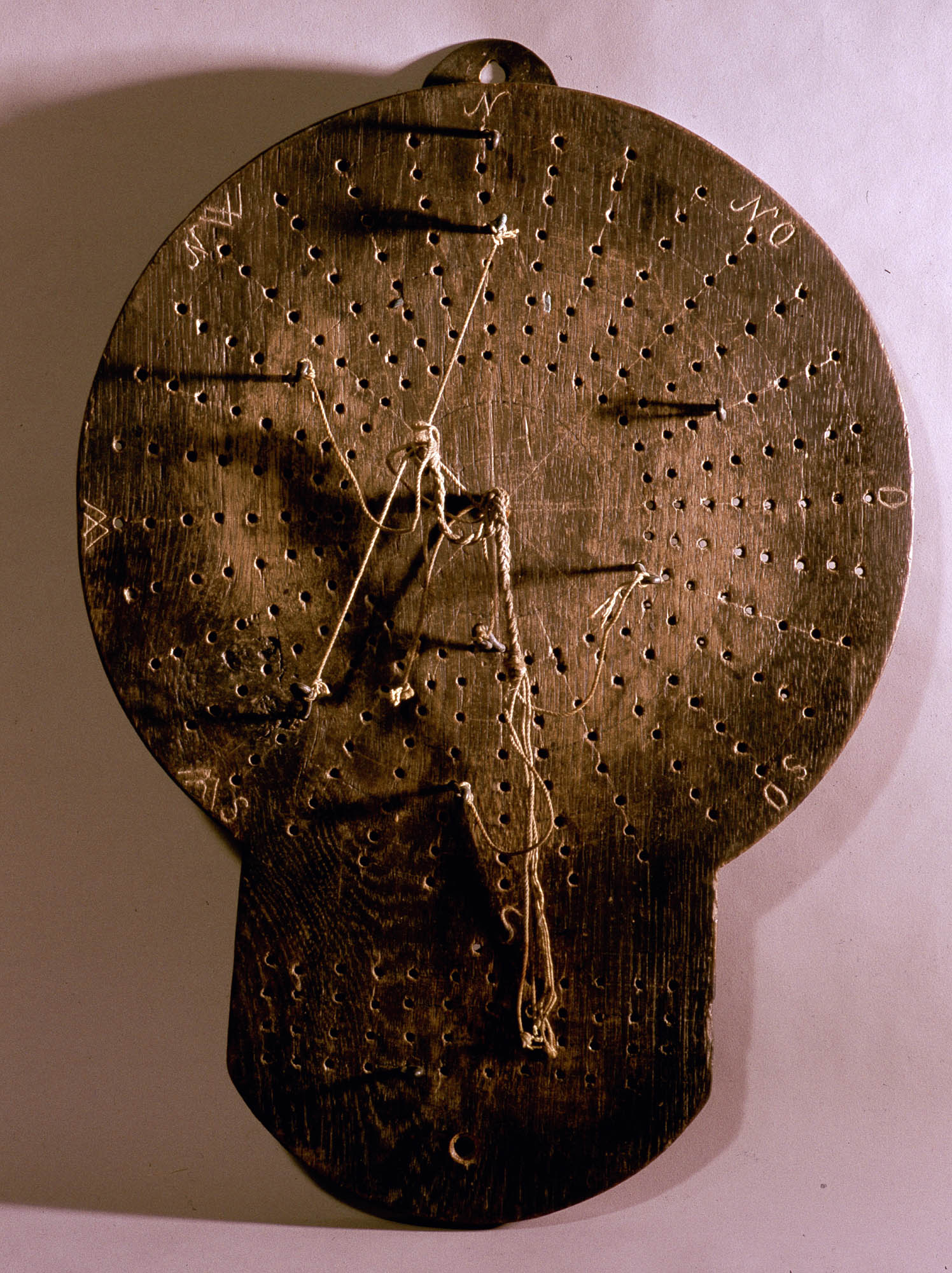 A circular wooden board with holes and pegs connected by strings.