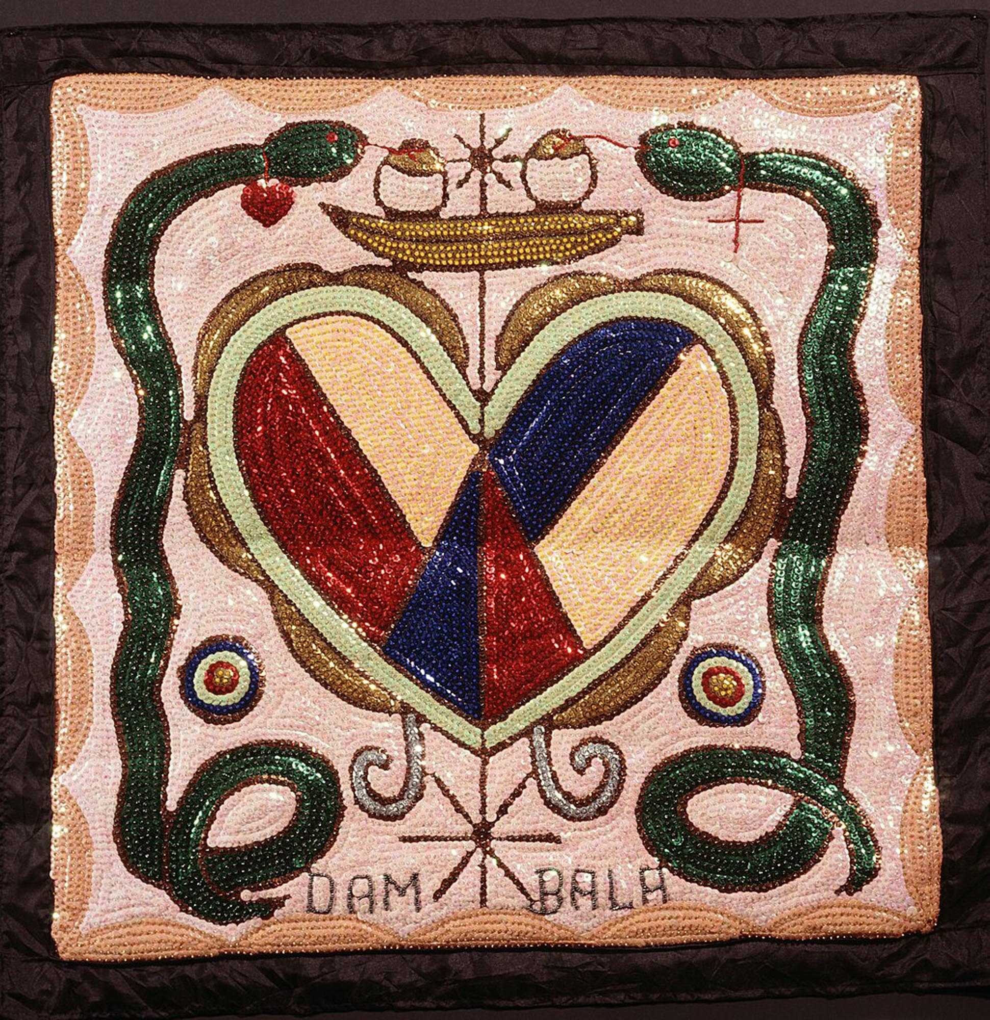 A Haitian Vodou flag, known as a Drapo, the flag is intricately crafted with sequins and beads on fabric, featuring two green snakes converging above a large, sequined heart divided into colorful sections. Above the snakes, a small golden boat-like vessel holds two offerings. Below the central heart, the name "DAMBALA" is spelled out in sequins.