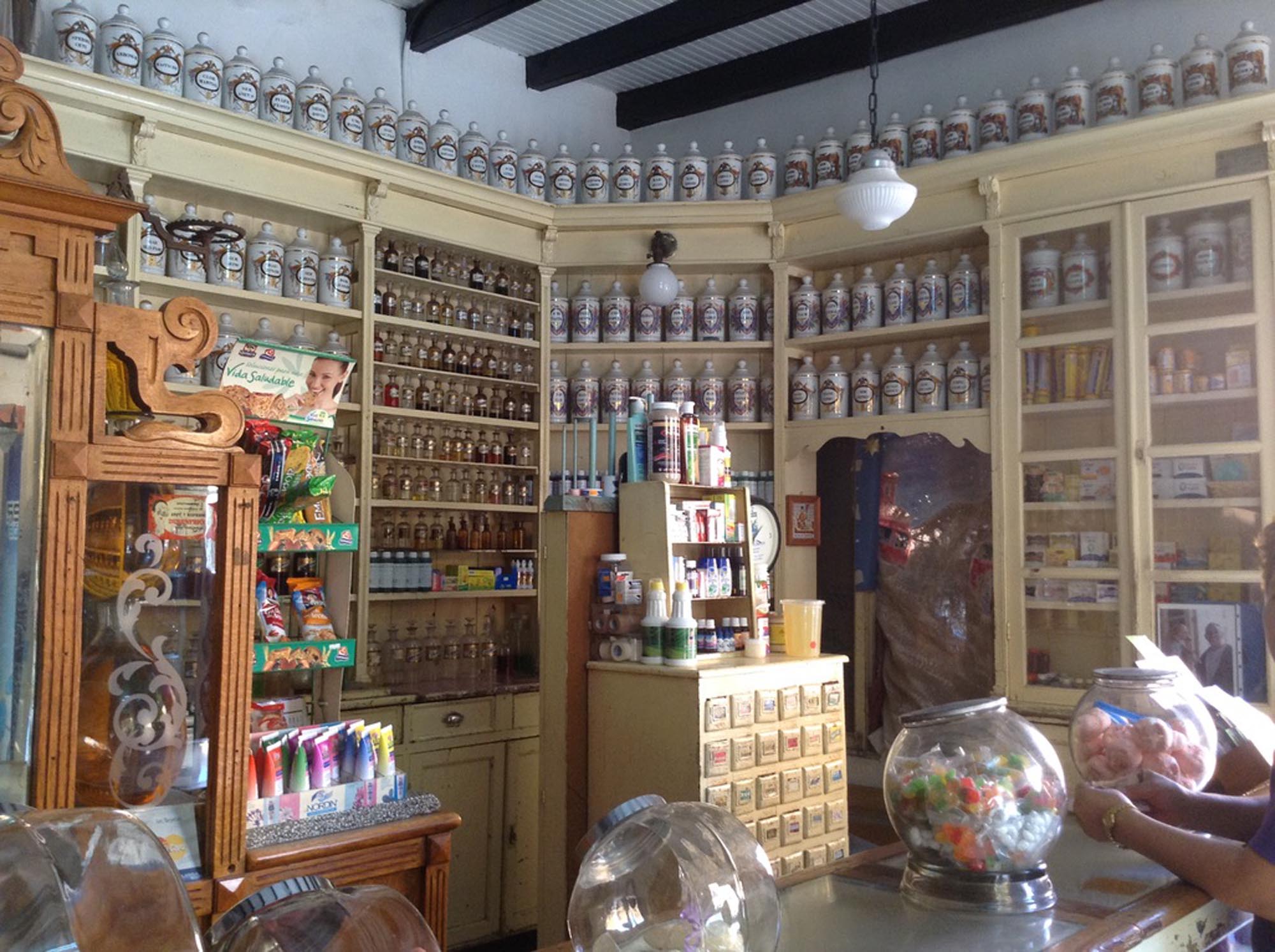 The interior of a historic apothecary located in Mexico. The establishment is well-preserved and features wooden cabinetry filled with numerous ceramic jars and bottles.