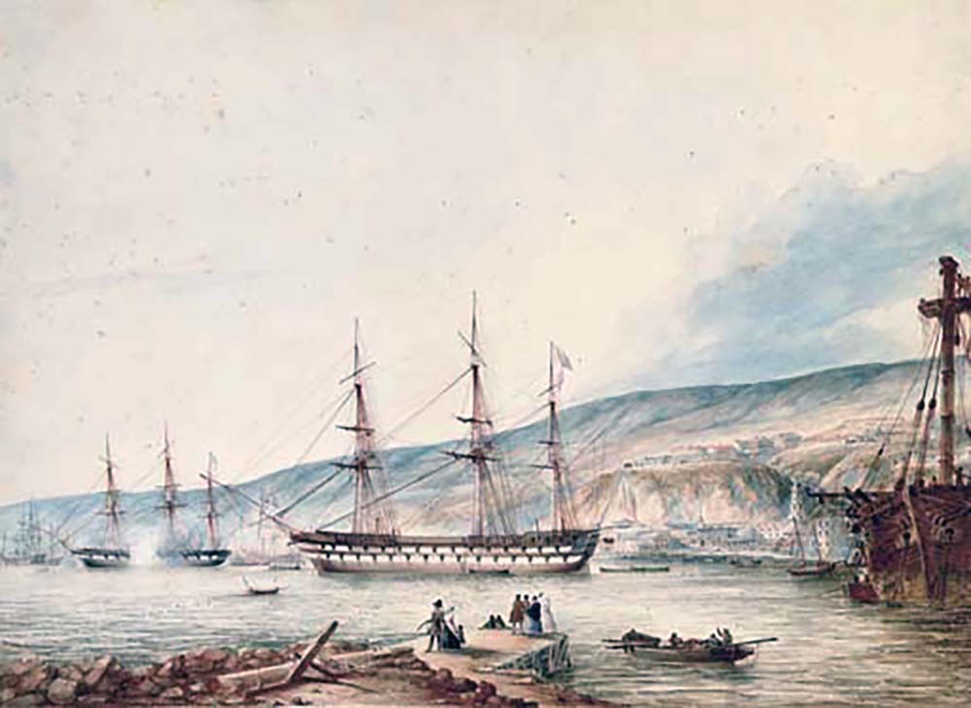 A watercolor painting depicting a bustling harbor scene with several sailing ships and figures on the shore. In the background, a town with buildings stretches along the base of a hilly or mountainous landscape.
