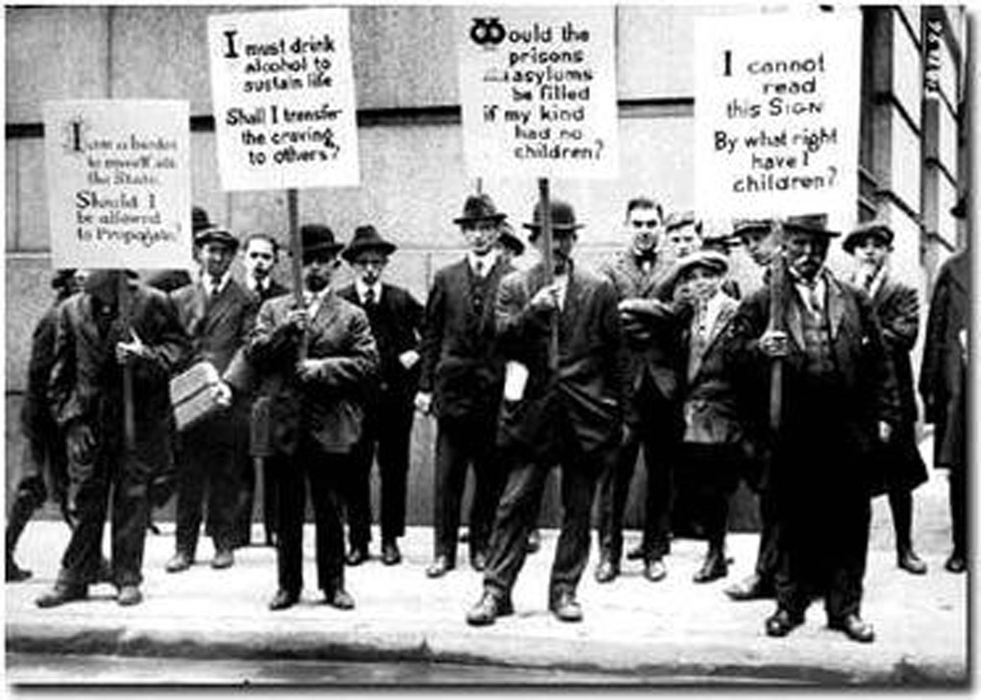 Photograph shows a group of men, standing on the street holding signs.