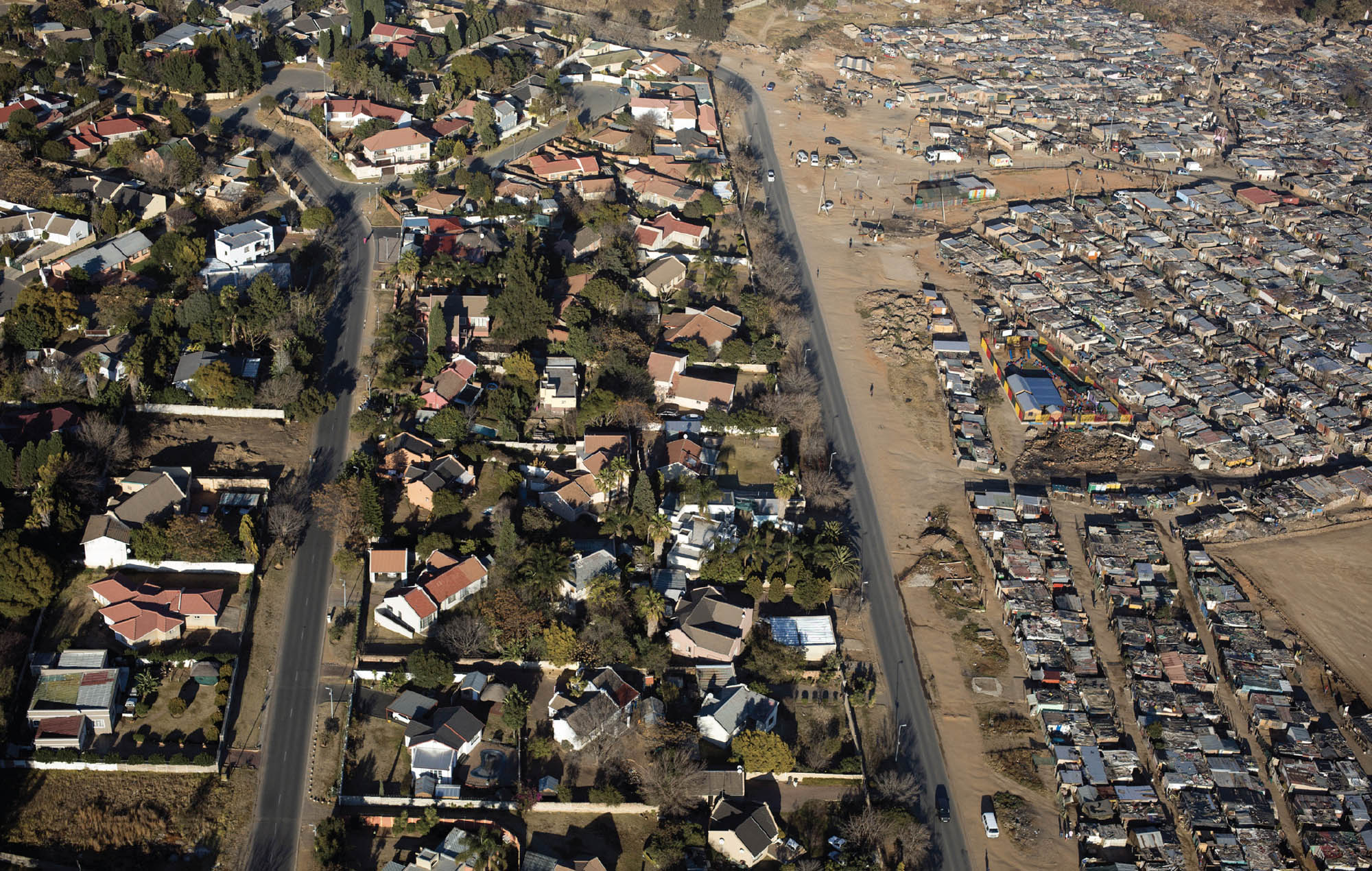 Image of an ariel view of two neighborhoods in Johannesburg. On the left is a well-developed area full of green spaces and homes. On the right is a poorly developed area, crowded with homes on a barren landscape.