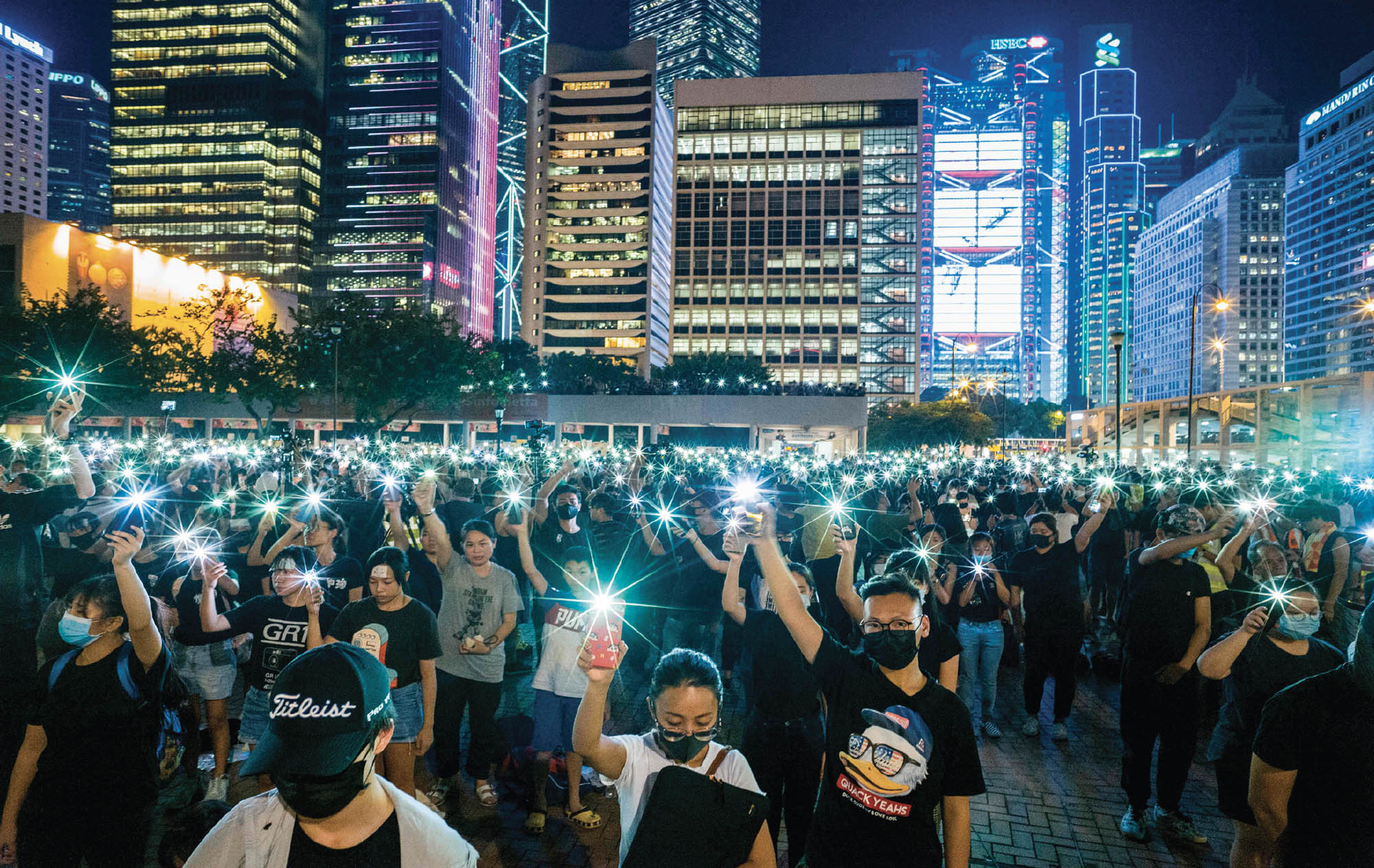 Image of a crowd of protestors wearing black and holding their phone flashlights up in the air.