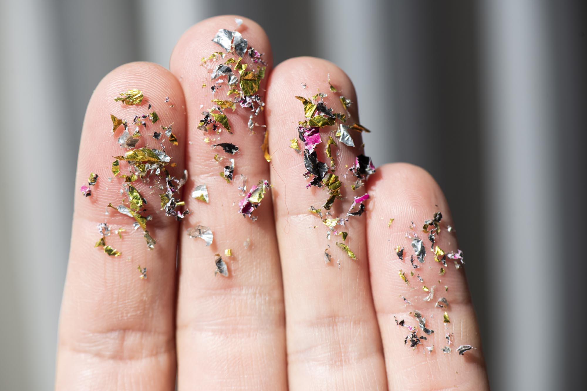 A close-up shot of several human fingers covered in colorful, shiny flakes resembling glitter but which are microplastic fragments.
