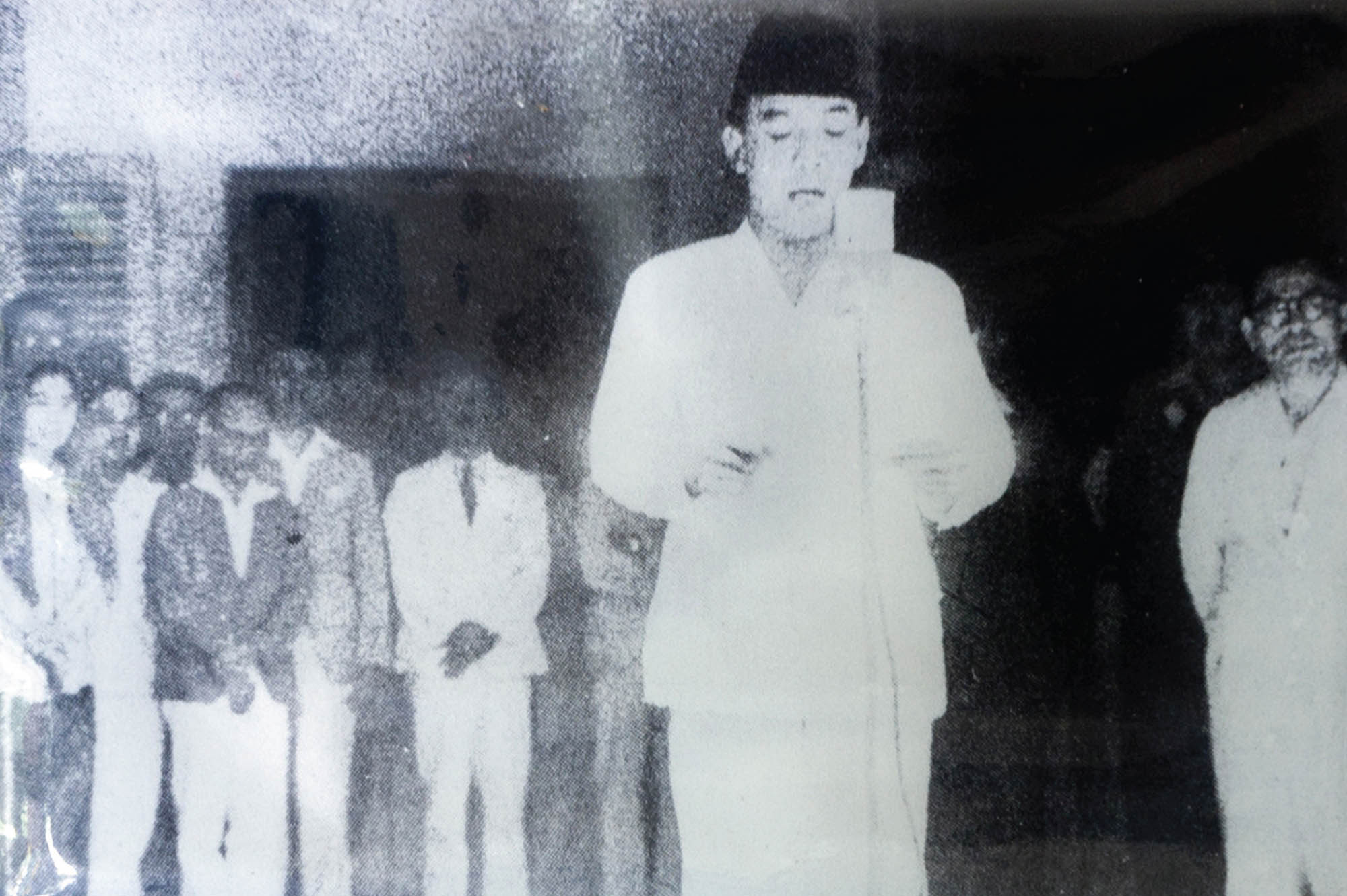 Photo of Sukarno, the first president of Indonesia, proclaiming independence. A crowd of supporters are gathered behind him.