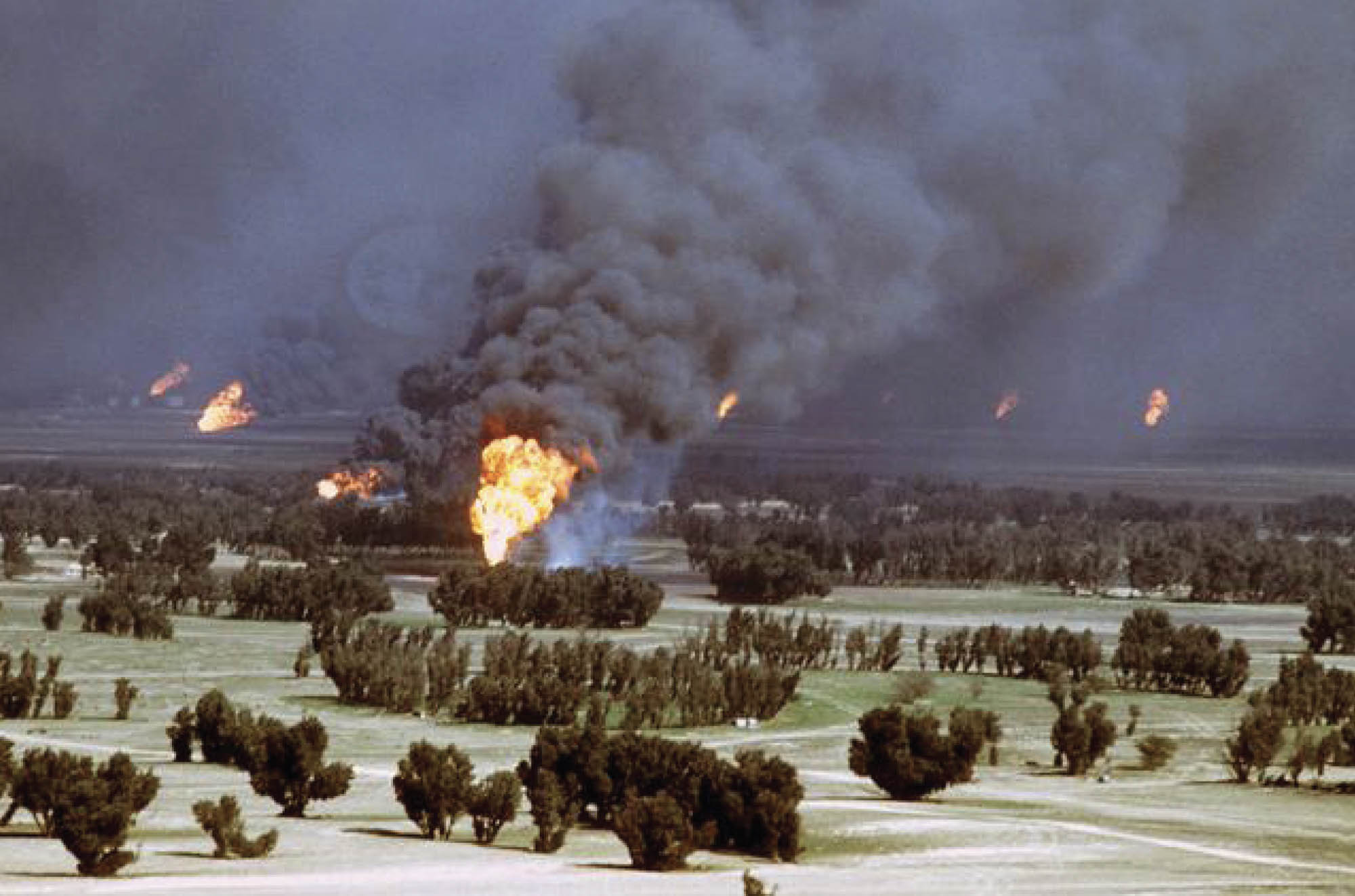 Photo of Iraqi oil fields burning. Large fires emit thick smoke throughout the field.