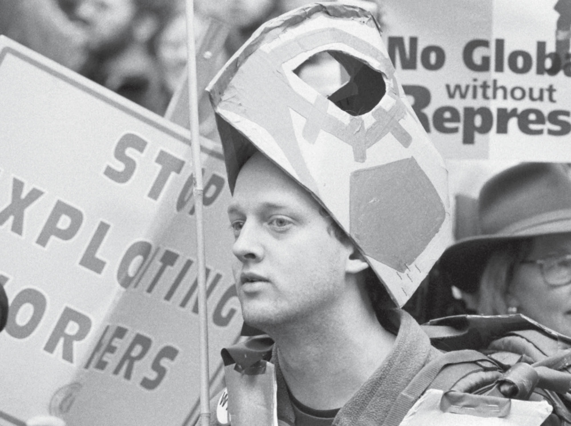 A photograph shows a man, wearing a handmade sea turtle helmet, is surrounded by other protestors carrying signs.