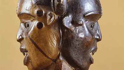 An elaborately carved sculpture featuring carved two faces on a small pedestal.