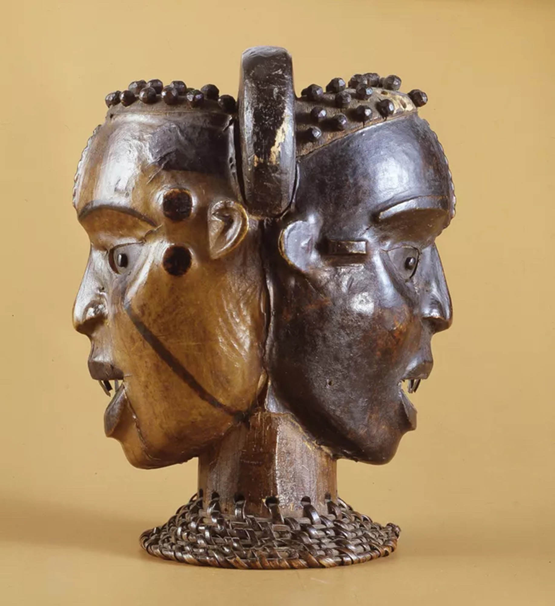 An elaborately carved sculpture featuring carved two faces on a small pedestal.