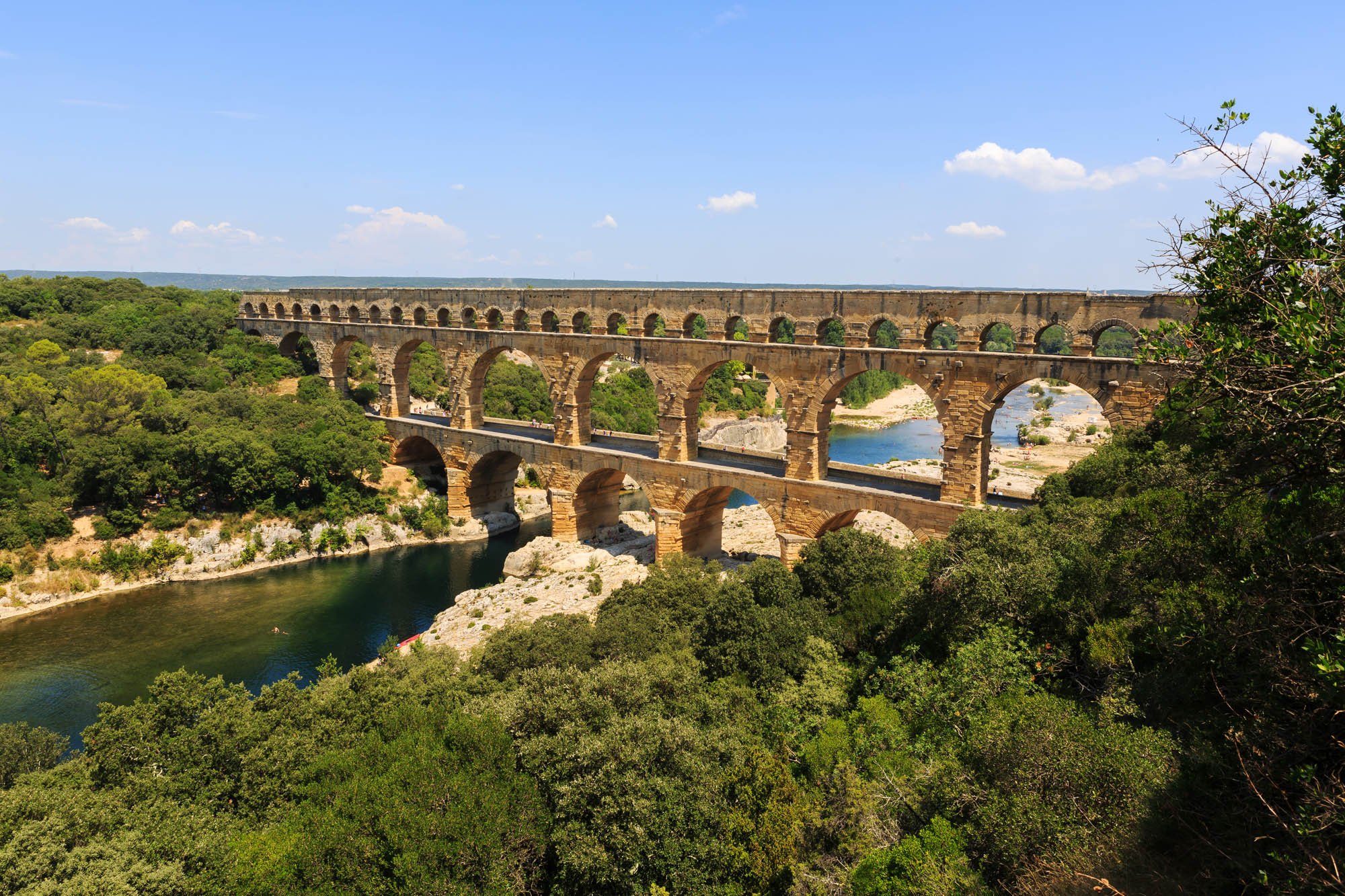 Pont du Gard aqueduct over water with trees and blue sky.