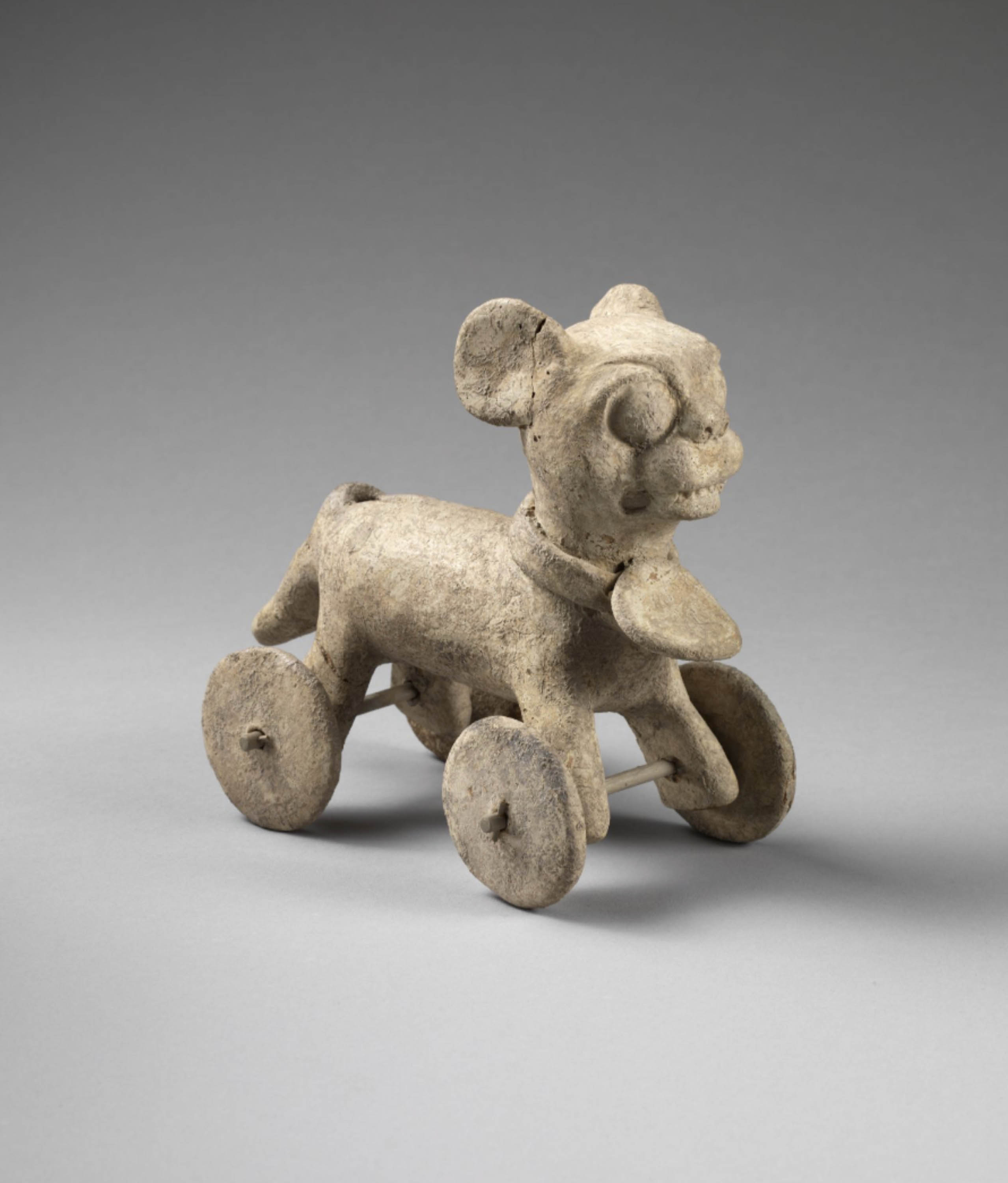 Small stone sculpture of a cat, with a collar. Wheels are attached to the cat’s feet.