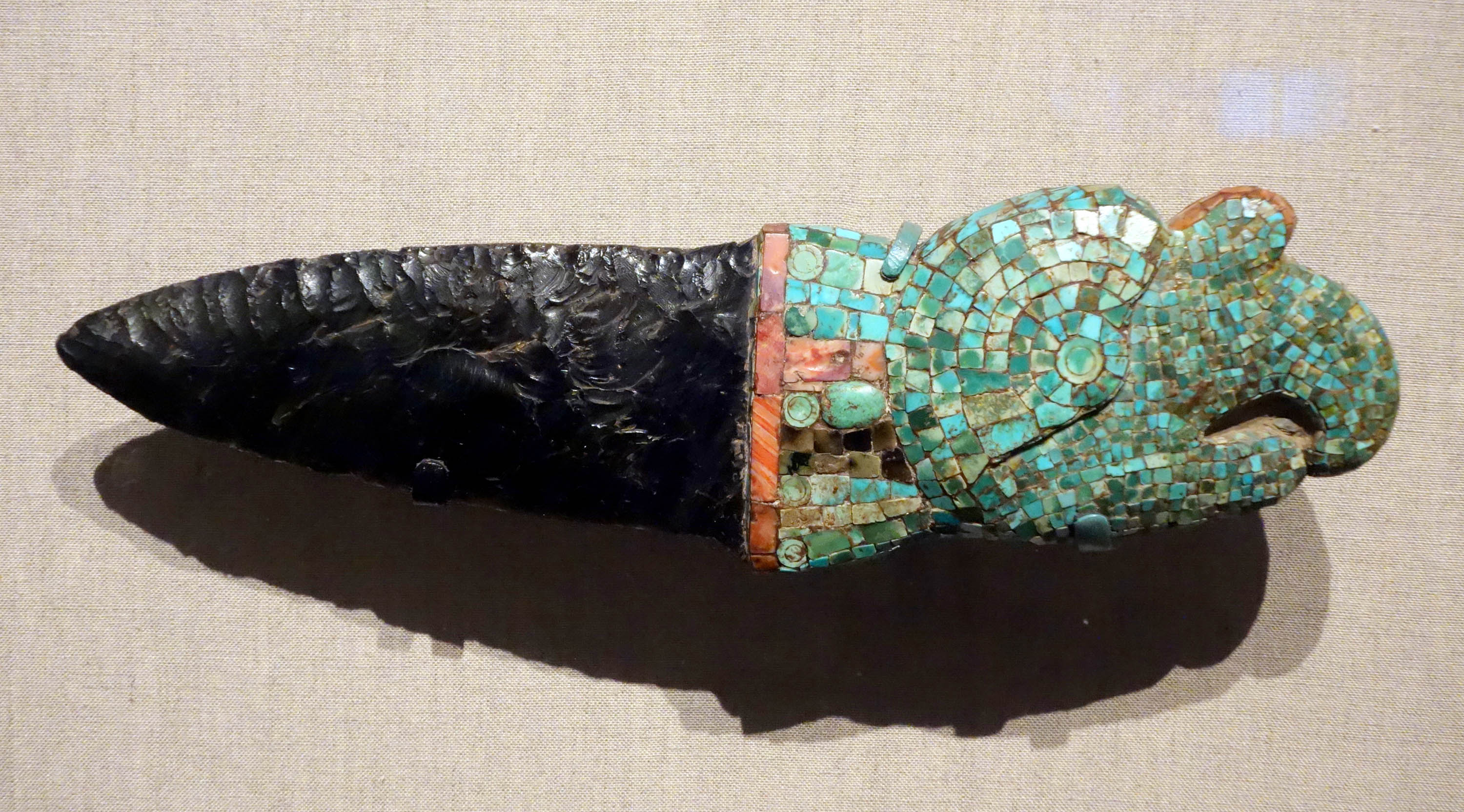 A knife carved from obsidian, a black, shiny rock. The handle is covered in a turquoise mosaic.