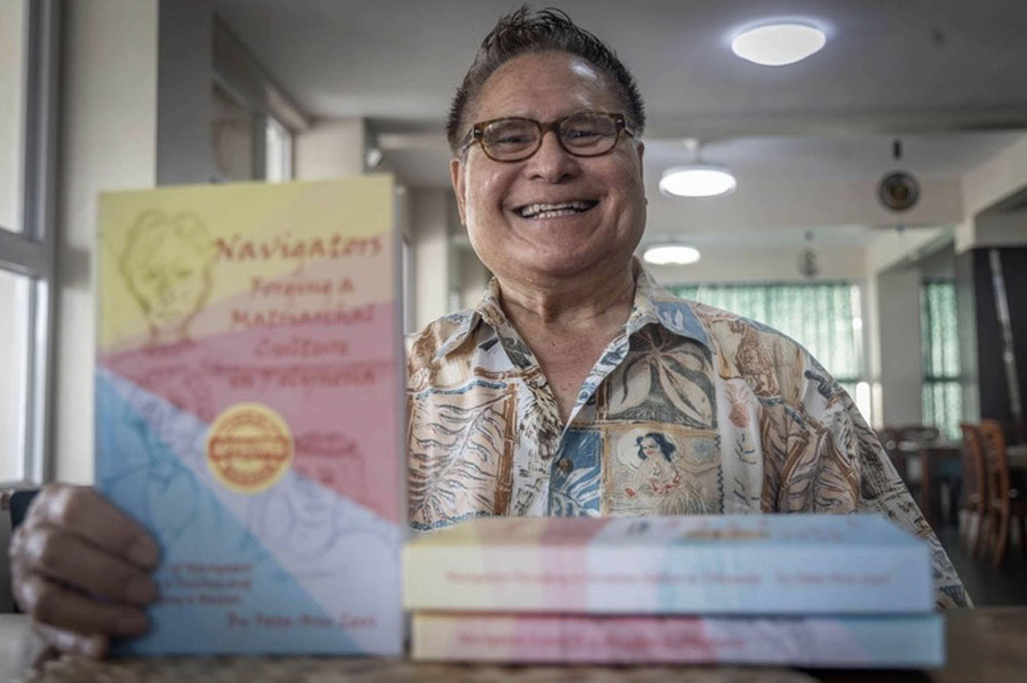 The author holds up his book about Pacific Ocean navigation and smiles at the camera.