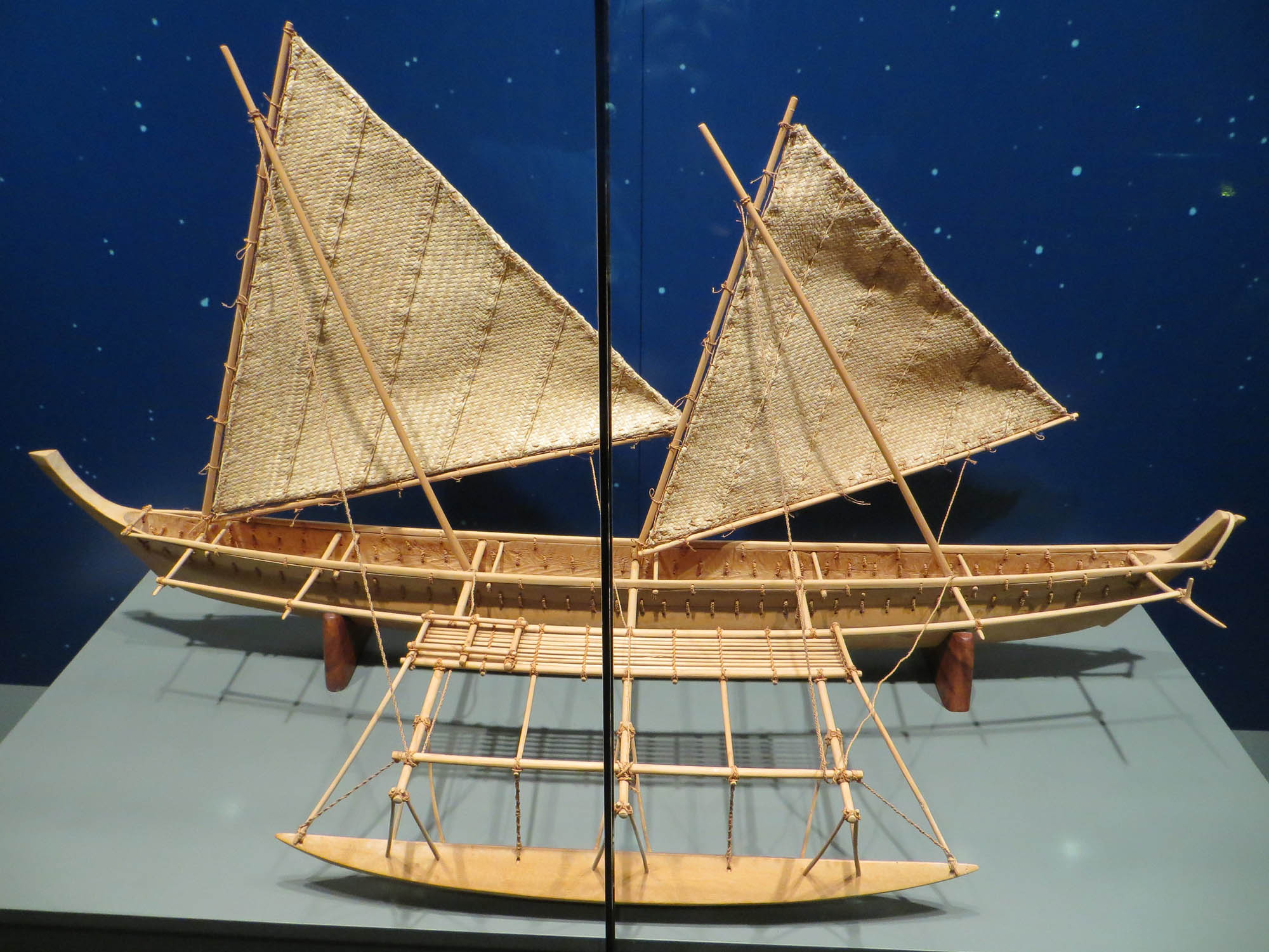 A model of a Polynesian sailing canoe with triangular sails and outrigger.