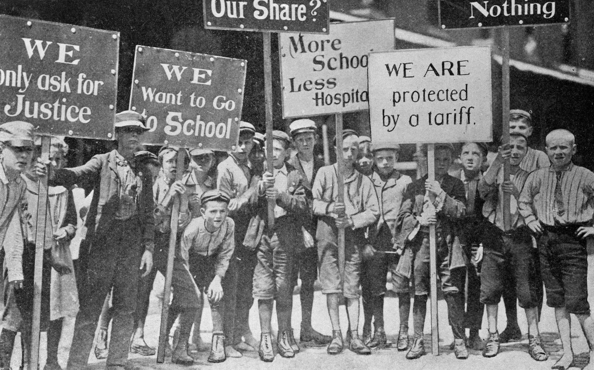 A crowd of boys protesting and holding signs asking for justice and for the chance to go to school.