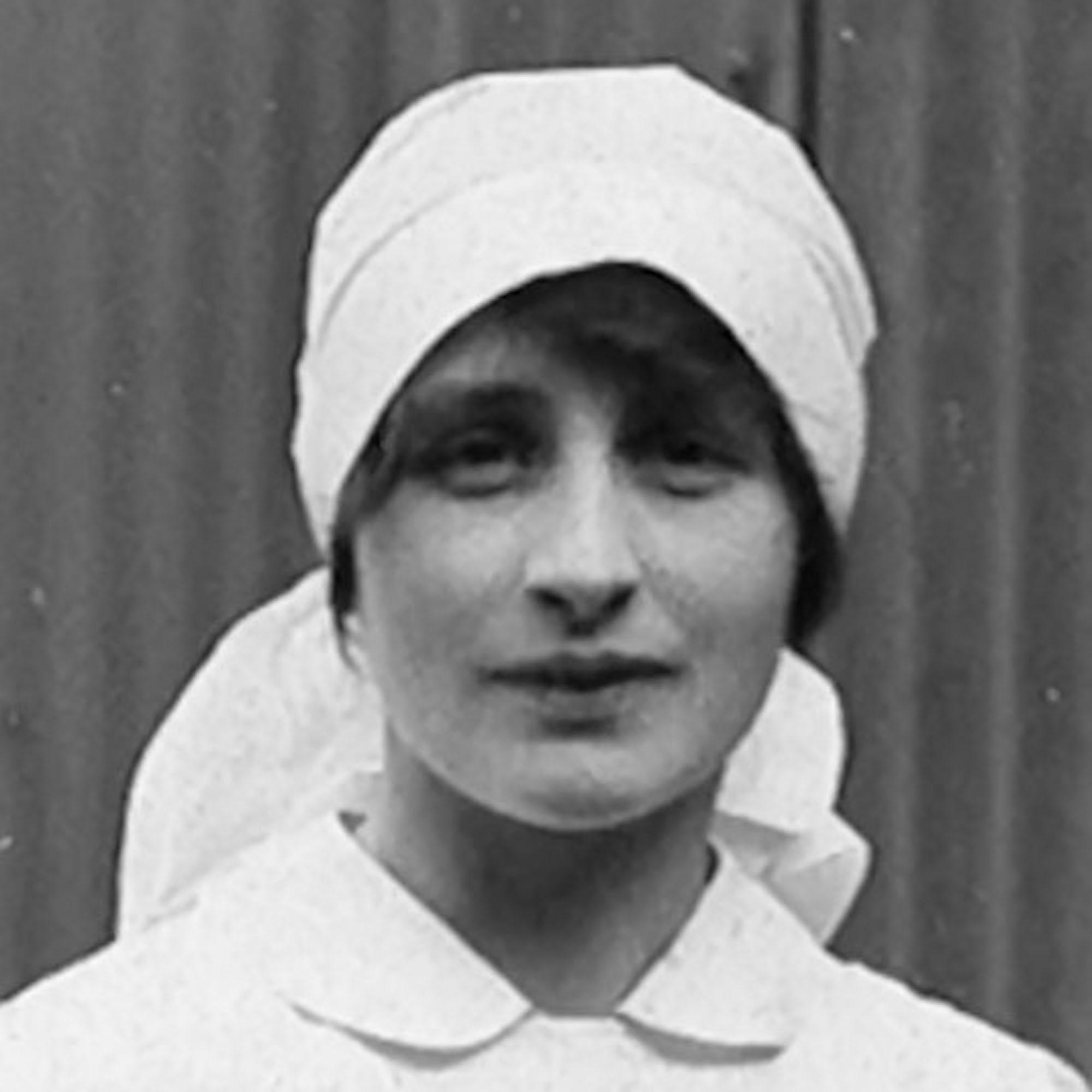 A black-and-white portrait of a woman in a nurse’s uniform, wearing a head covering and collared garment, facing the camera.