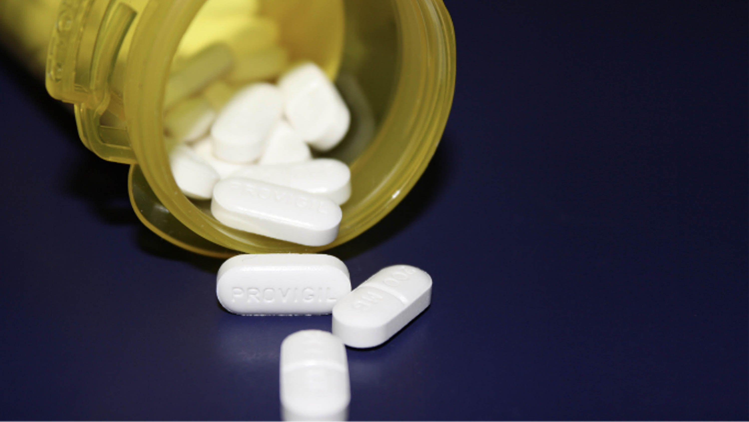 A plastic pill bottle lies on its side and several pills are spilling out.