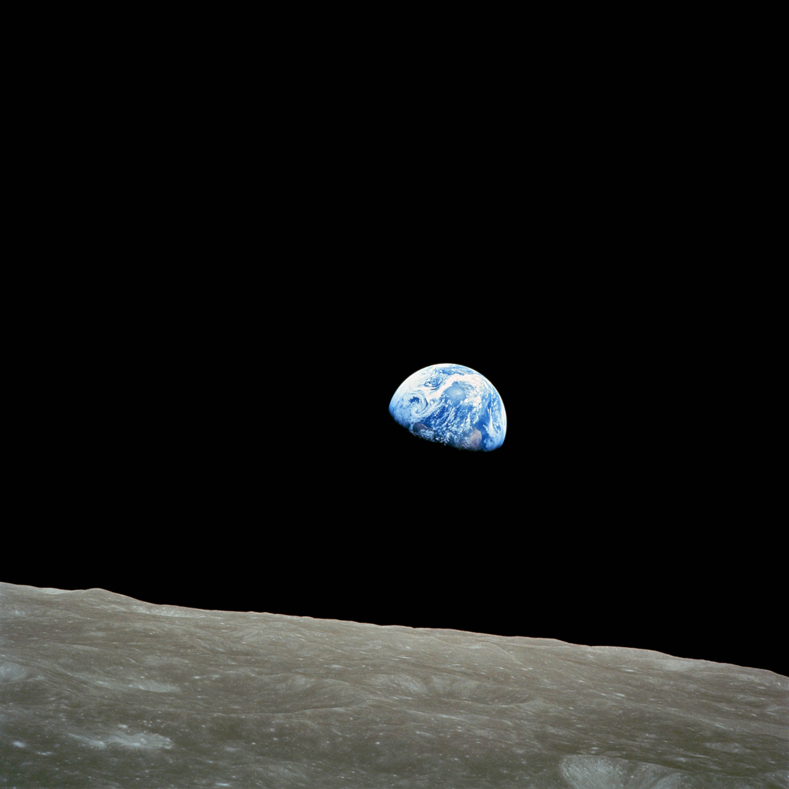 Photo of Earth rising over the Moon’s horizon, taken from space, showing Earth’s blue and white surface against a black sky.