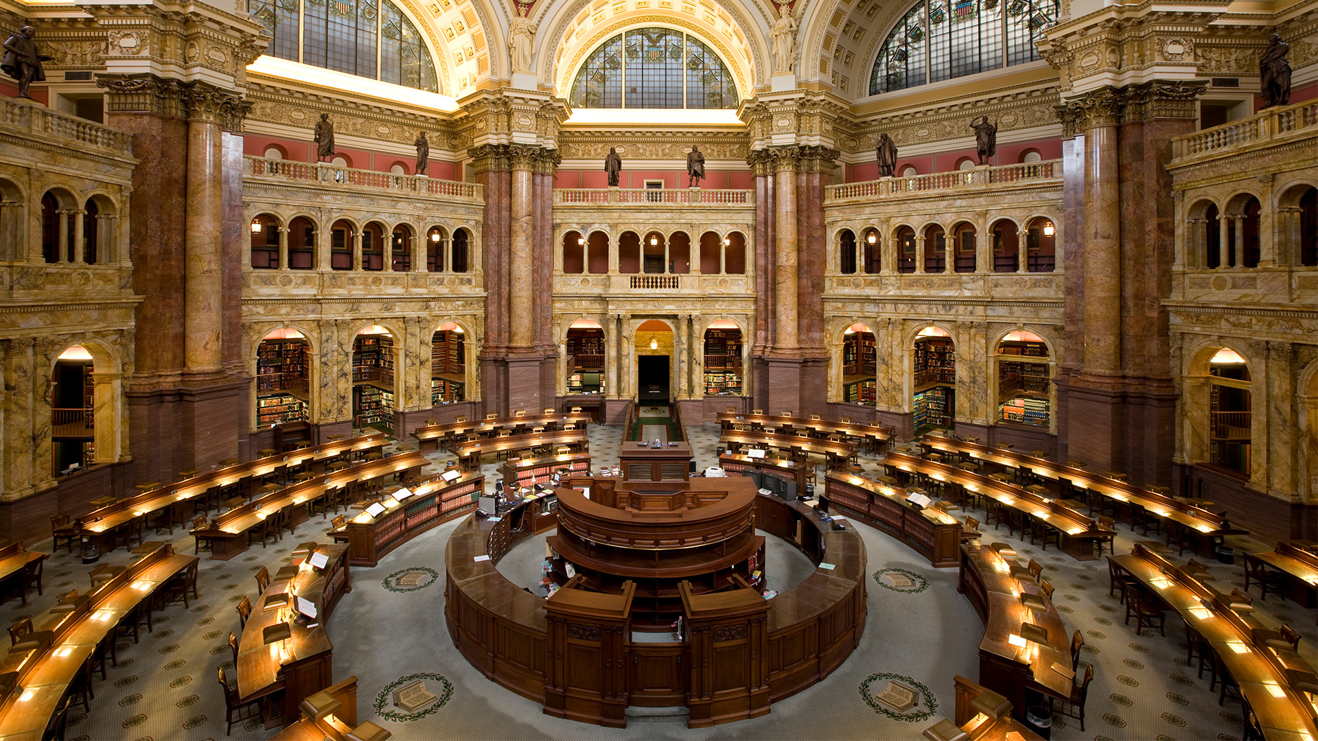 A view of the reading room in the Library of Congress, with circular reading desks surrounding a central dais.