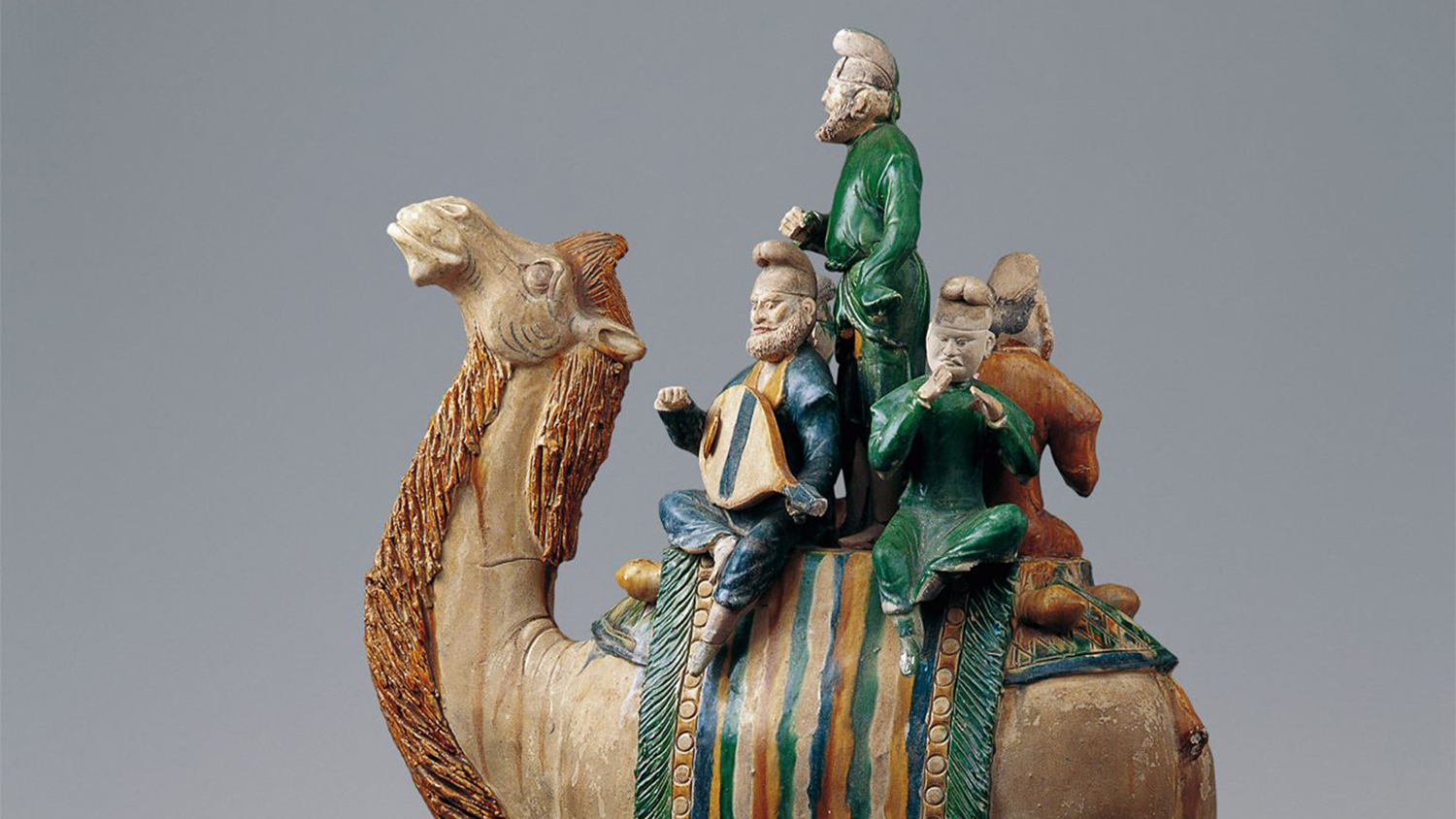 A porcelain sculpture of four men in ancient Middle Eastern apparel sitting on the back of a large camel.