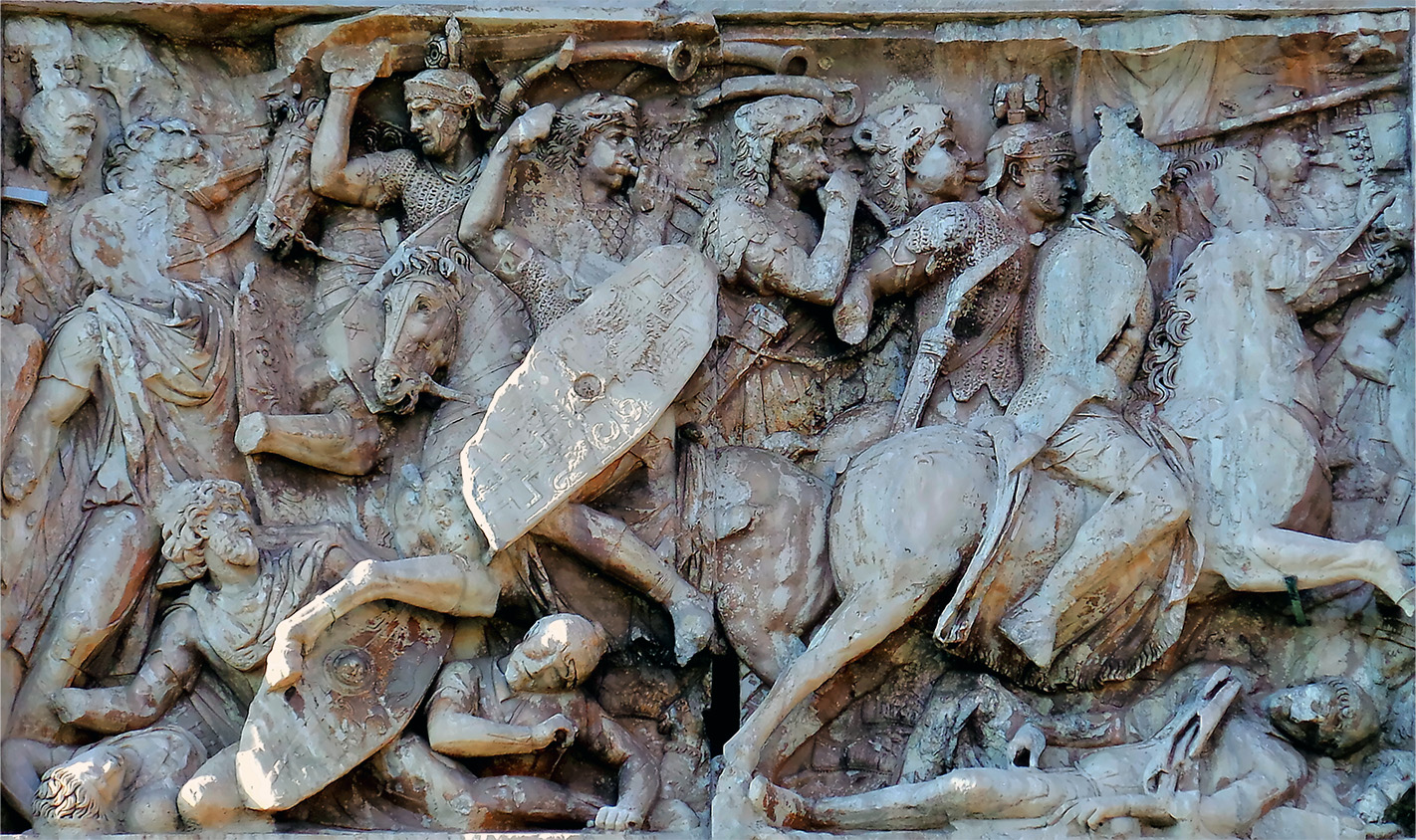 A stone relief carving of mounted Roman soldiers fighting fallen enemies in battle.