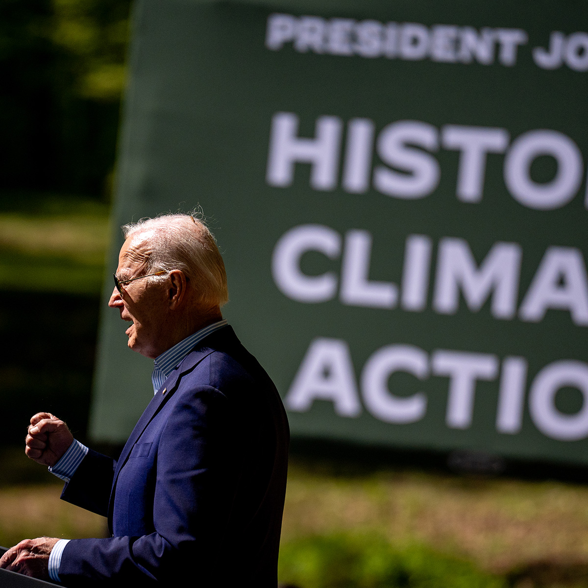 President Joe Biden stands at a lectern and speaks at an event. In the background, a banner reads Historic Climate Action.