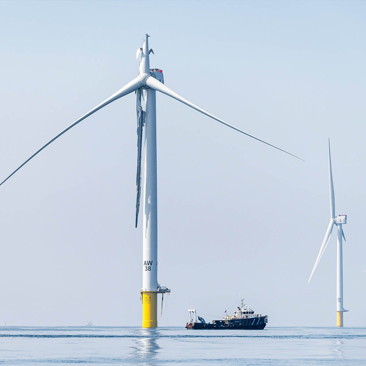 Workers on a tugboat inspect a broken blade of a wind turbine out at sea.