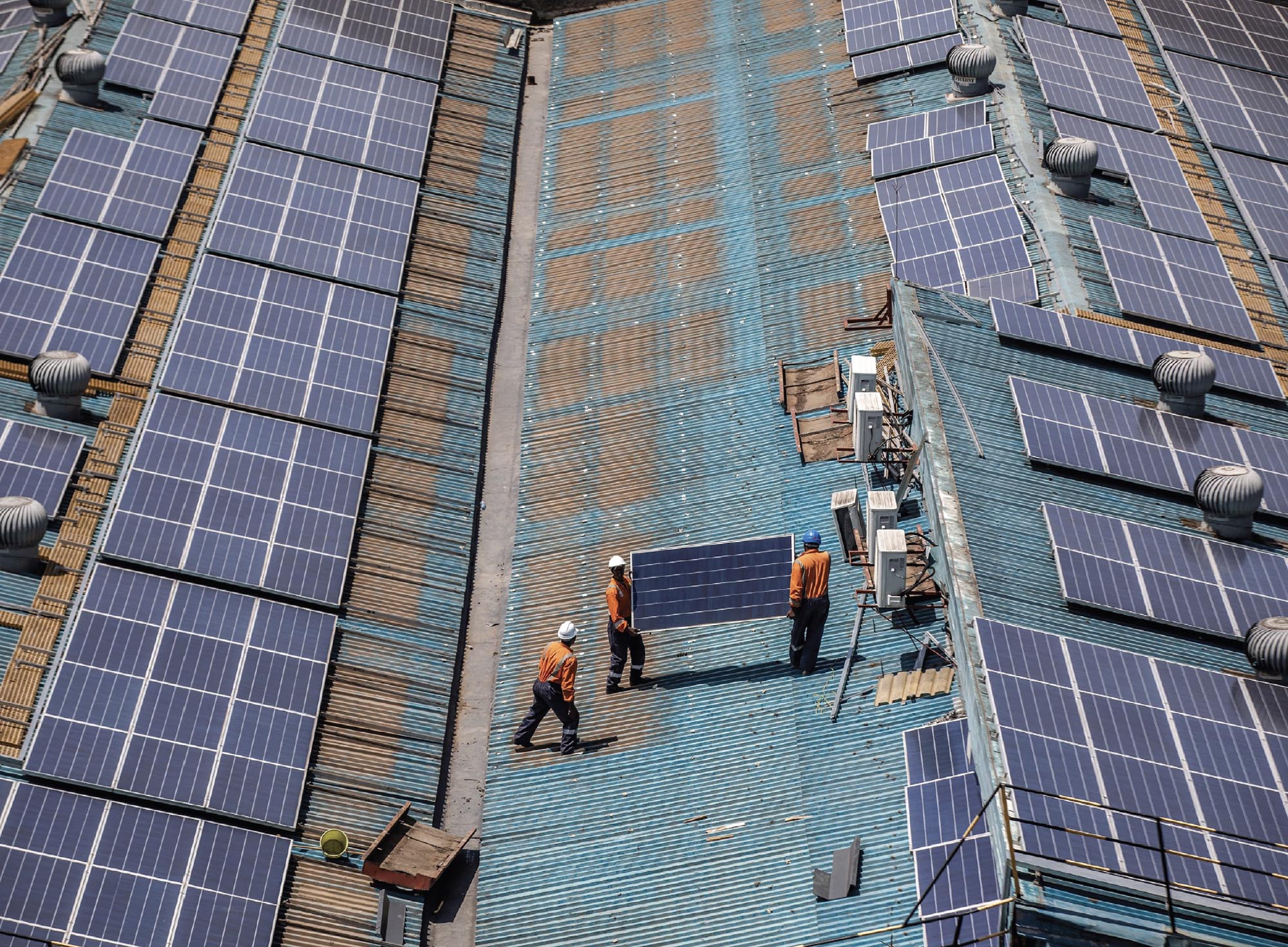 Technicians work on the maintenance of rooftop solar panels at a partially solar-powered factory.