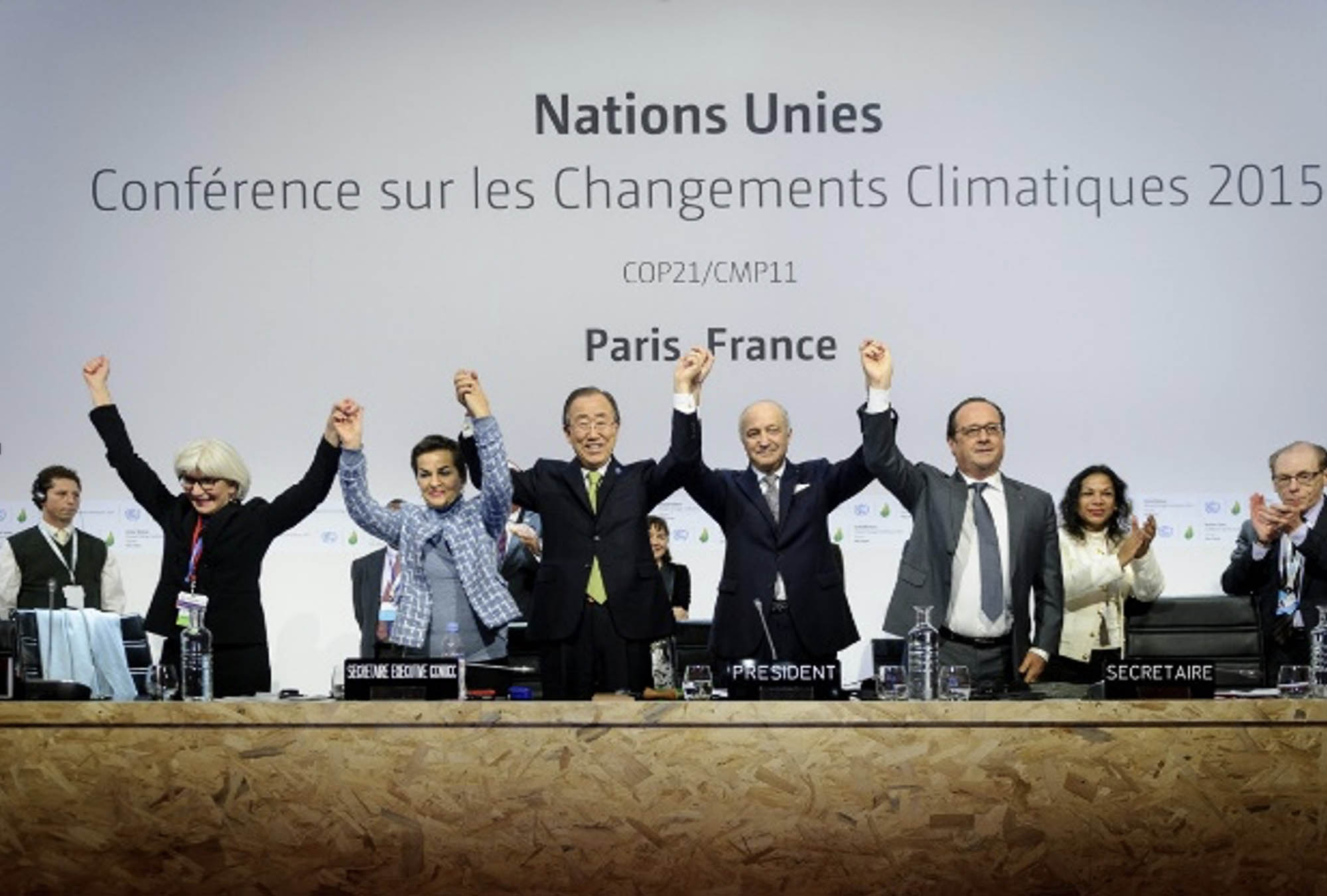 A group of lawmakers on a stage raise hands together after adoption of a historic global warming pact at the COP21 Climate Conference.