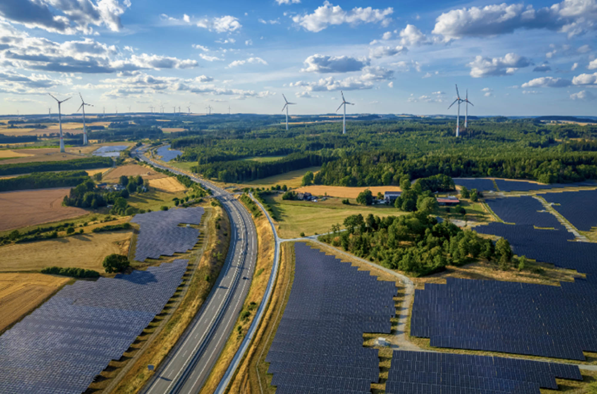 Aerial view of a solar farm and wind turbines near the highway road interchange.