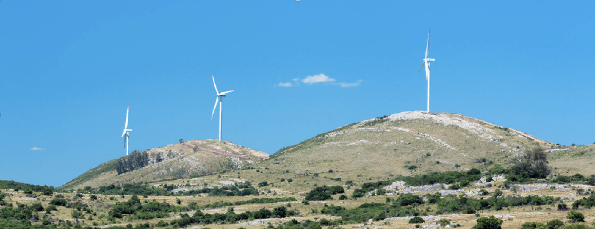 Windmills perched high on a rocky hilltop against a clear sky.