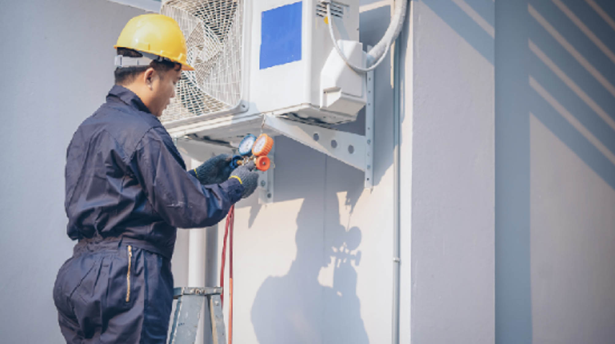 A photo of a technician wearing safety equipment and repairing an air conditioner unit.   