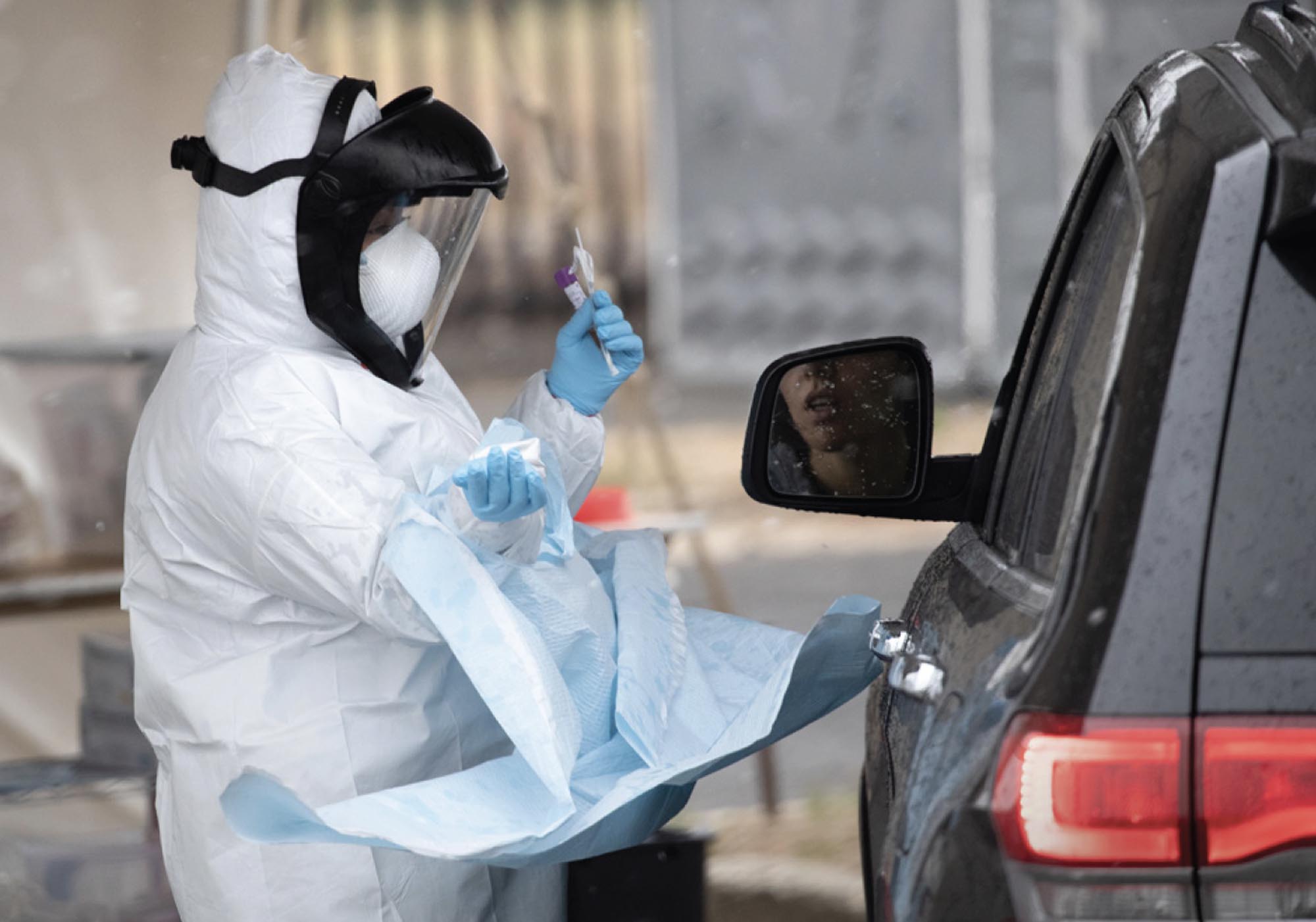 A nurse dressed in personal protective equipment prepares to give a coronavirus swab test