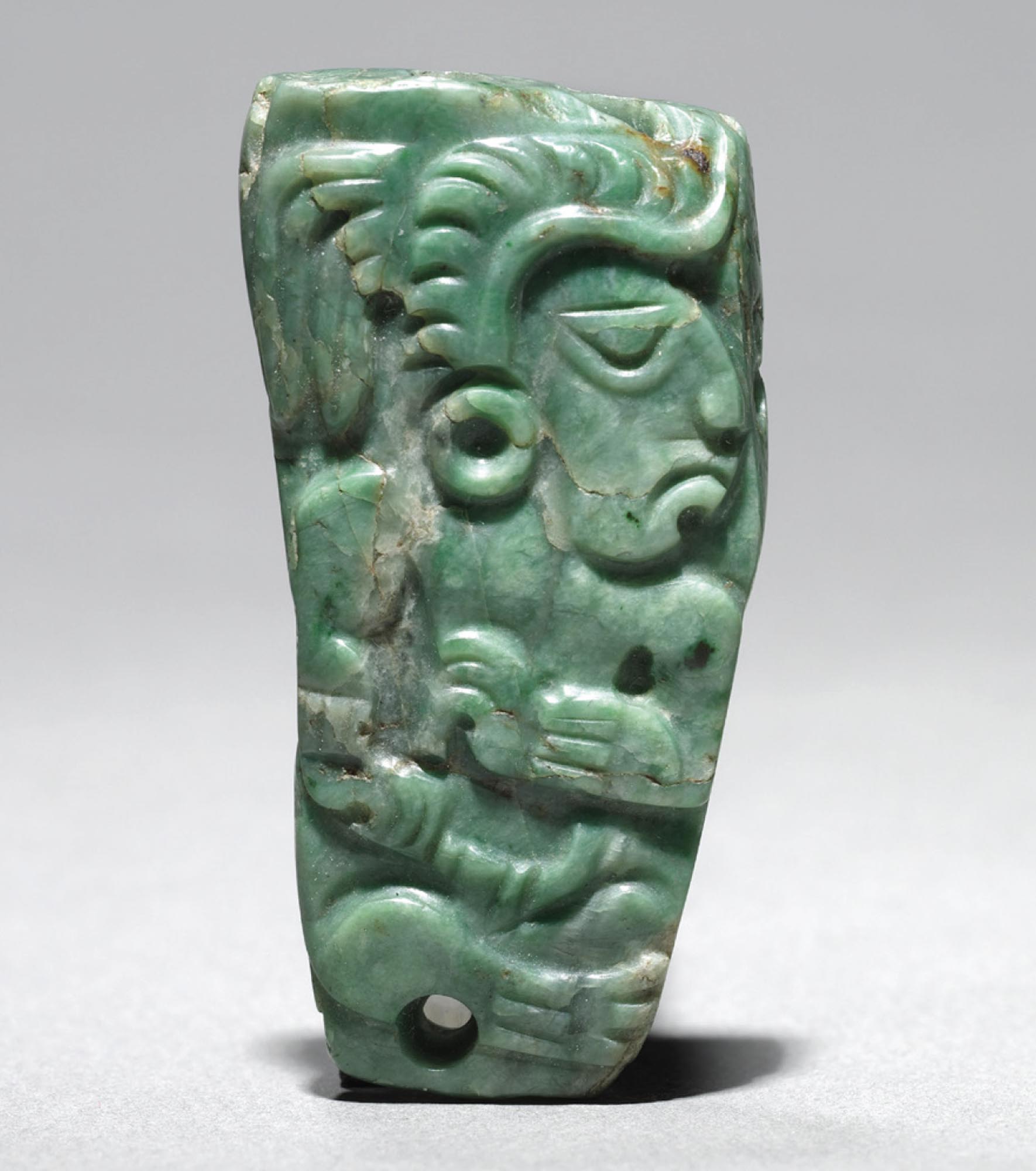 A green jade ornament with a profile view of a Mayan figure carved into it.