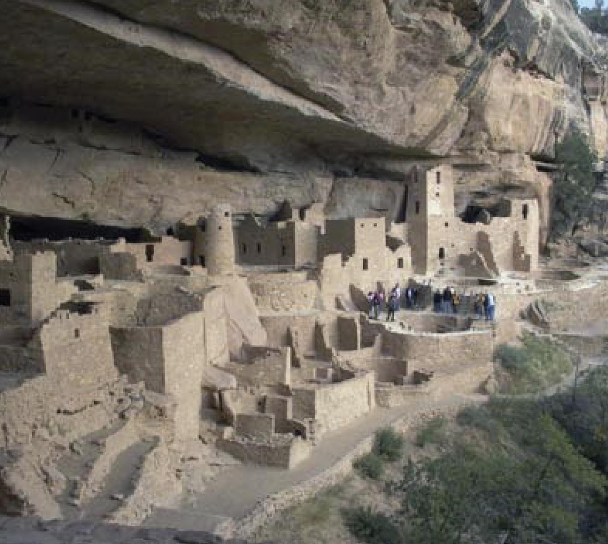 Stone buildings built underneath a towering cliff at the Mesa Verde National Park.