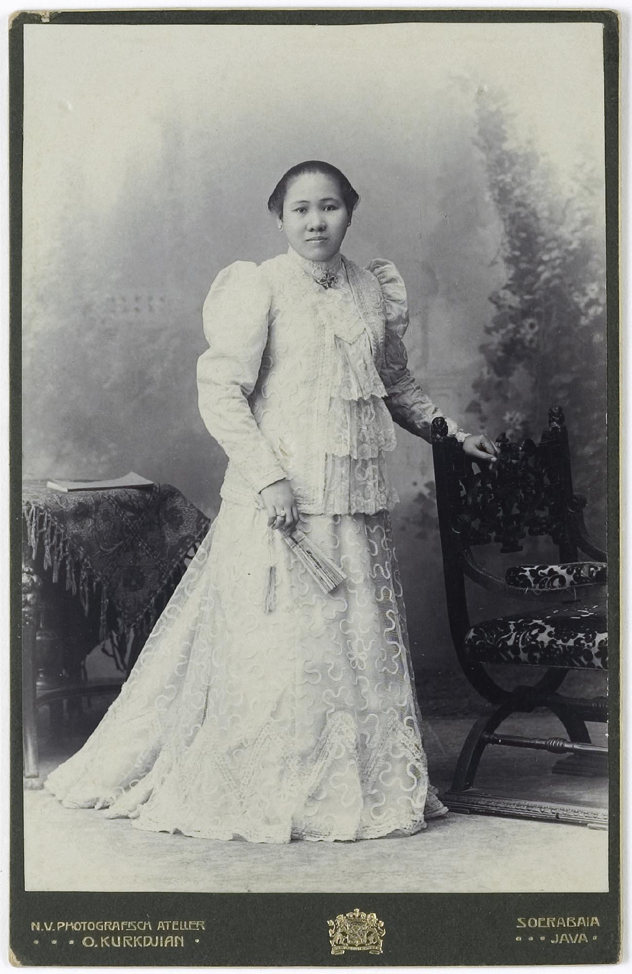 Formal portrait of a woman in a long, white dress holding a folding fan.