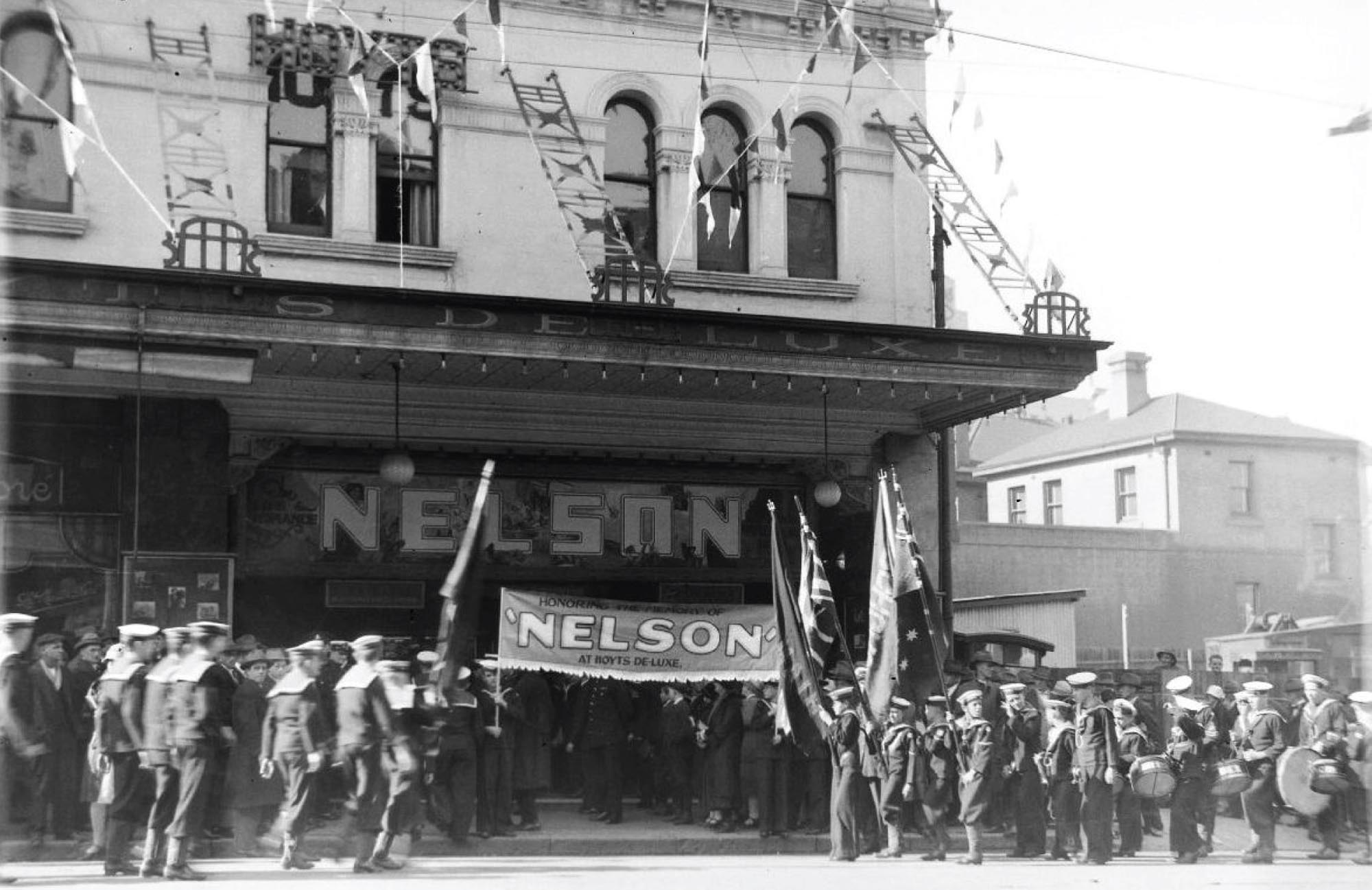 Marchers in the street carry musical instruments and signs lobbying  for an expanded navy and larger British Empire.