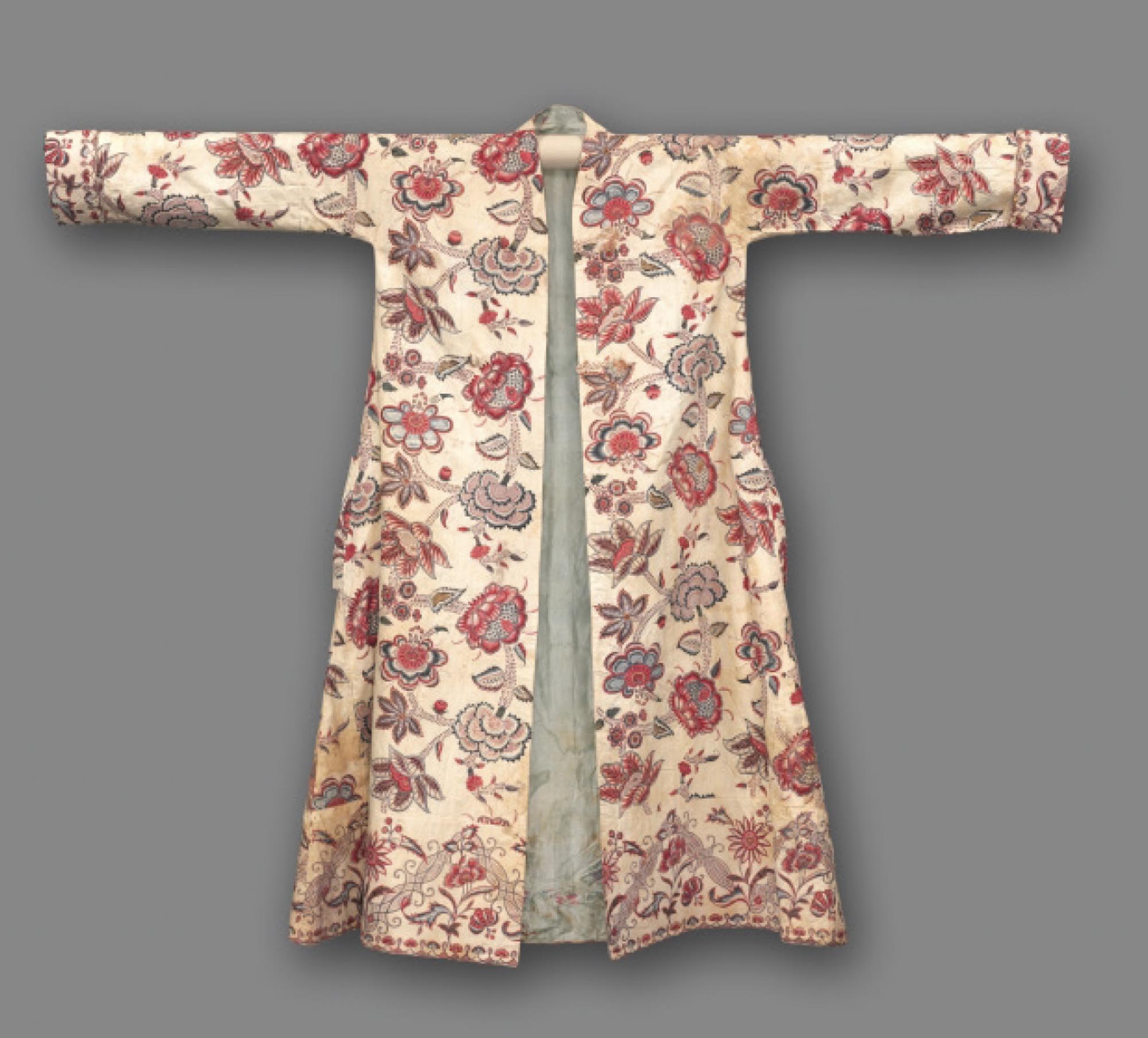 A colourful, long cotton morning coat decorated with flowers. This coat is made from textiles produced in India.