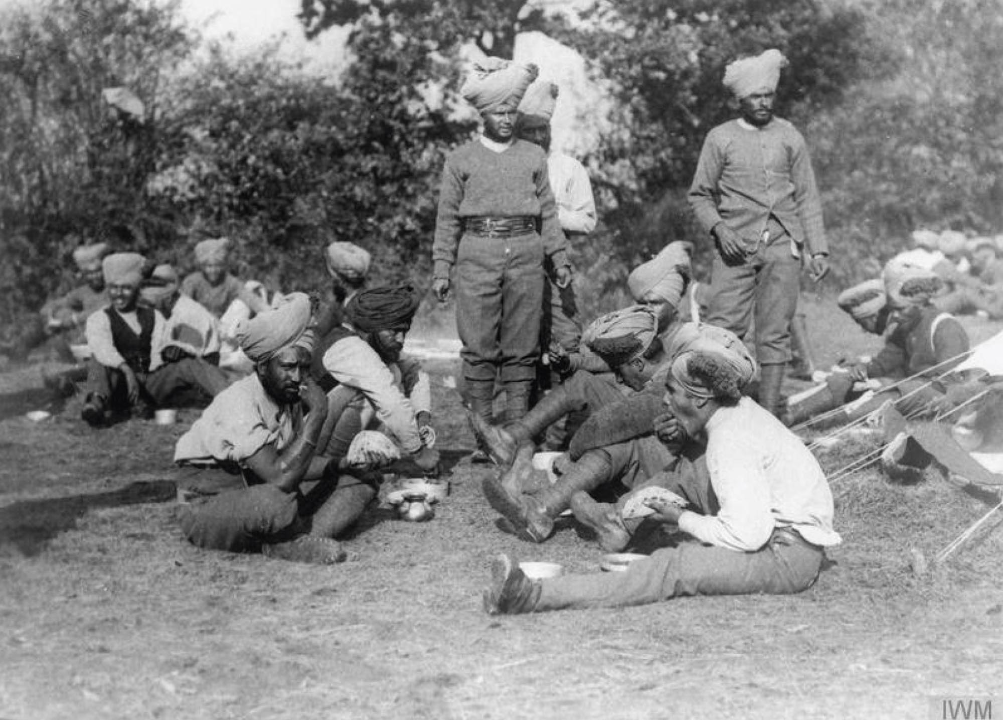 Soldiers sit and stand in a field, eating their lunch. Some are laughing and some hold a very serious expression.