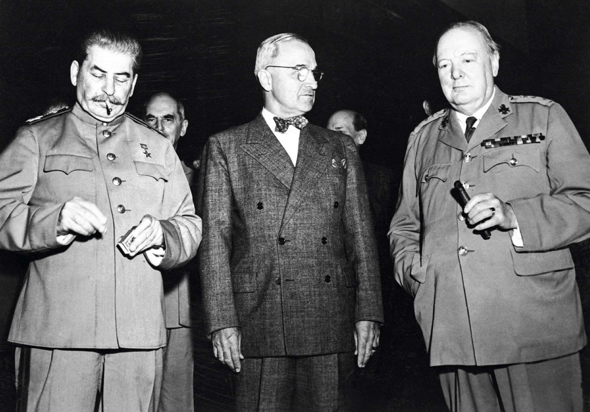 Black and white photo of Soviet leader, Joseph Stalin, US President Harry Truman, and British Prime Minister Winston Churchill. Stalin is lighting a cigarette.