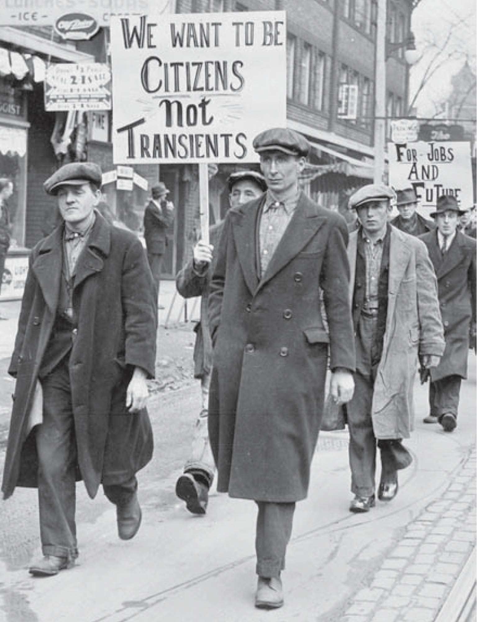 A group of unemployed workers march down the street holding protest signs.